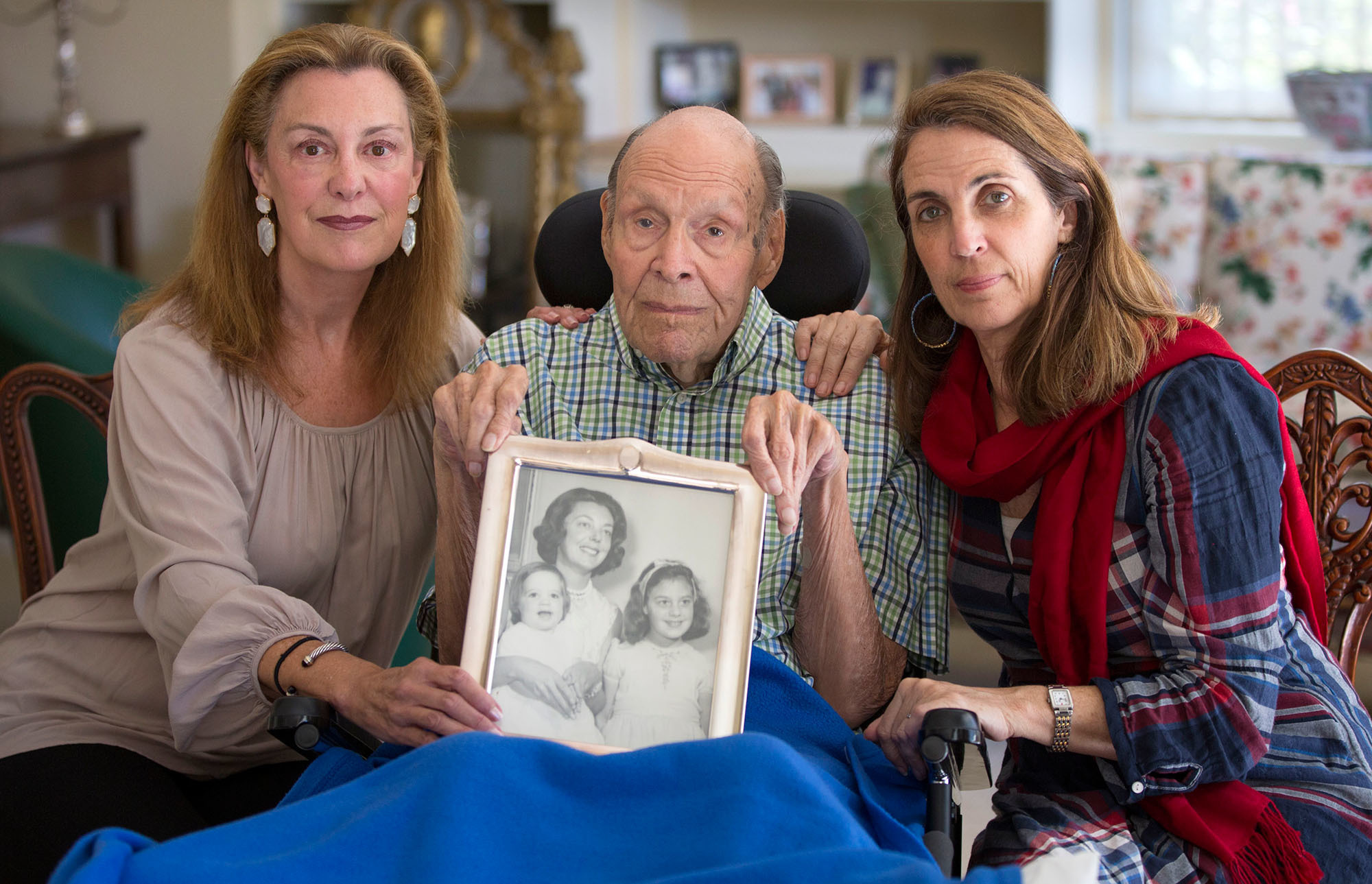 Laura Rees (left) and her sister Nancy Fee sit with their father, Joseph Fee, while holding a photo of his late wife, Elizabeth. (Robert Durell for KHN)