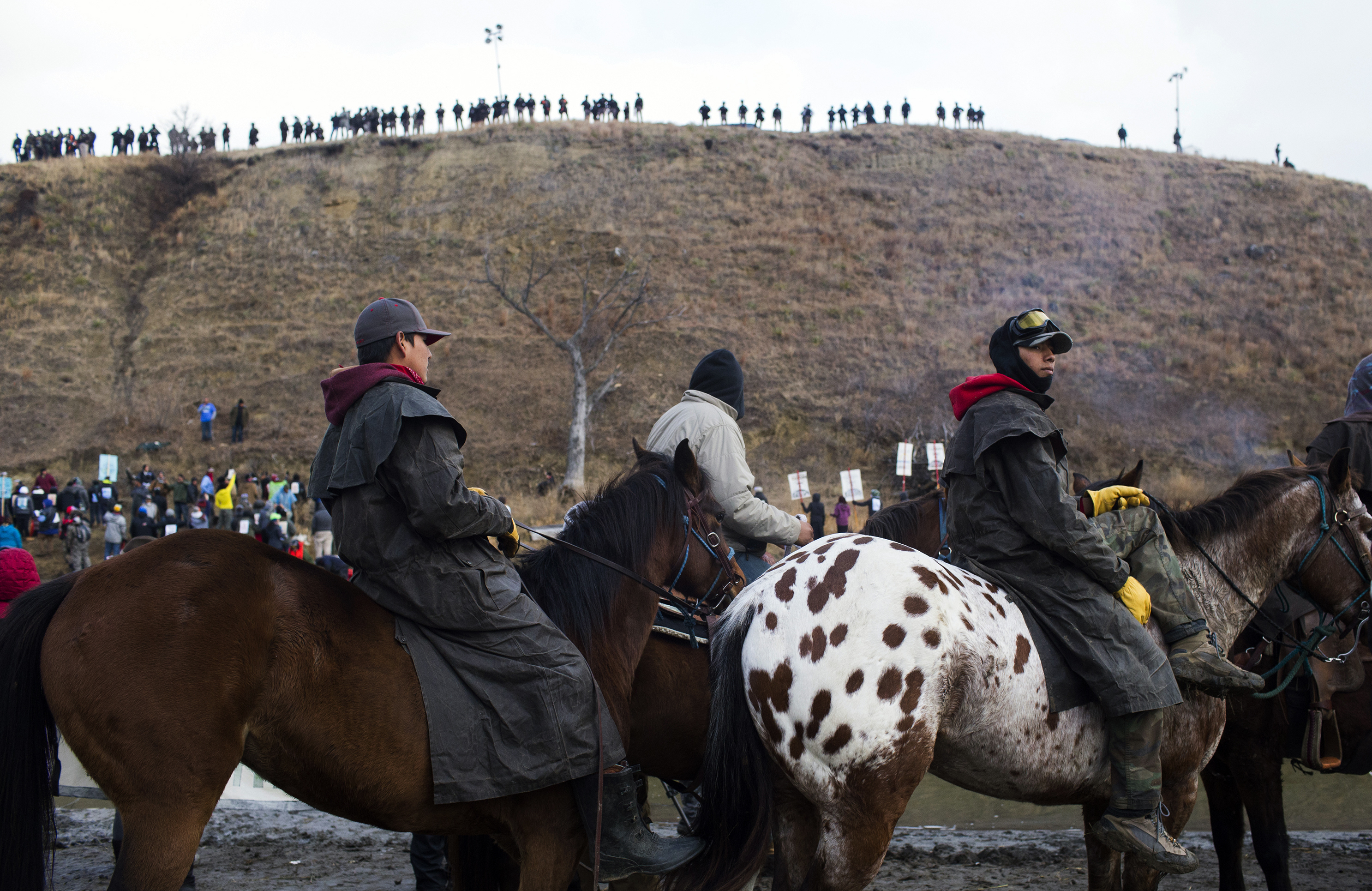 Protesters gather at Standing Rock Reservation on Thanksgiving Day to build a bridge to Turtle Island, which they consider sacred ground. Police are seen lining the island hill beyond them. (Cassi Alexandra for NPR)