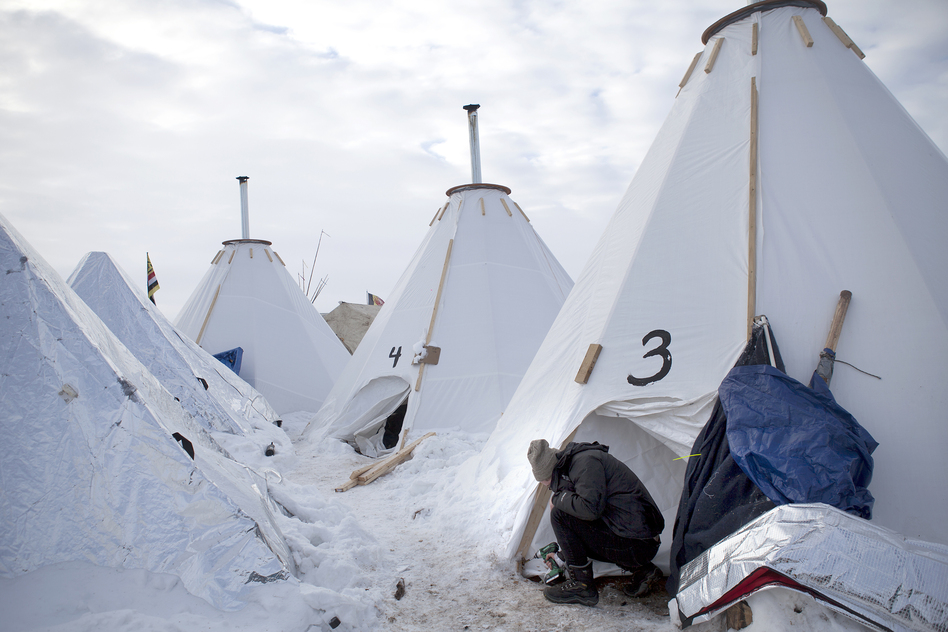 Jacob Brooks makes adjustments to one of the camp's many "tarpees," a winterized teepee made of tarp with a built-in chimney, designed by Paul Cheokoten Wagner. There are roughly 60 tarpees around various camps now, and Wagner has fundraised enough for another 20 more. (Celia Talbot Tobin for NPR)