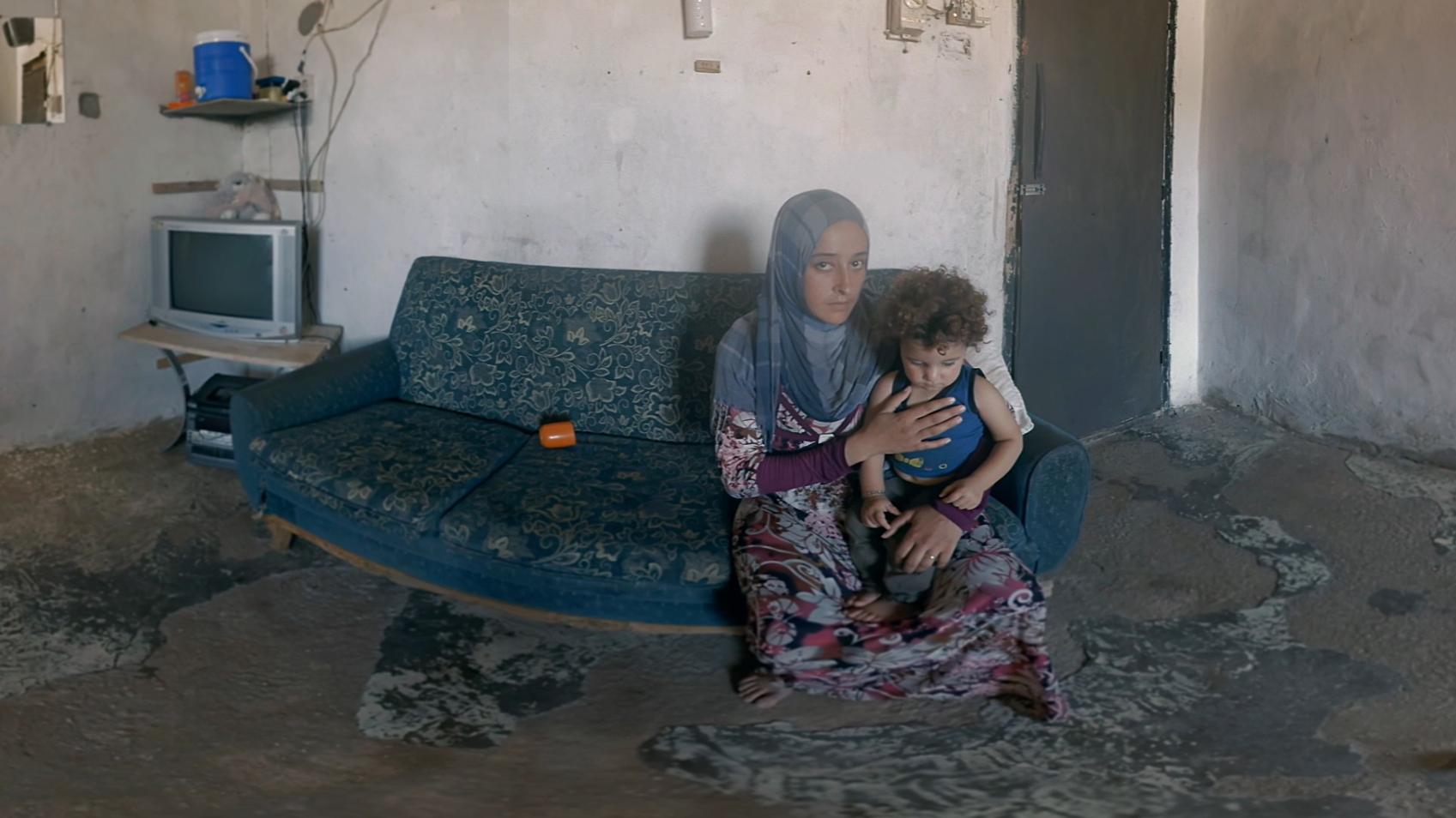 A Syrian woman and her child sit in their refugee living space in Lebanon. They are featured in Four Walls, <a href=&quot;https://www.rescue.org/four-walls#four-walls-vr&quot;>a virtual reality presentation</a> by the International Rescue Committee. (YouVisit Studios)