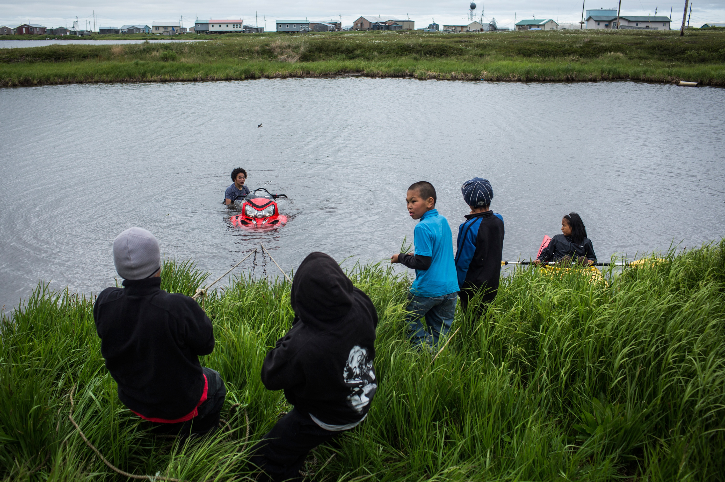 Alaskan Village, Citing Climate Change, Seeks Disaster Relief In Order To Relocate 2 Yup'ik children help recover a snowmobile that sank when its owner attempted to drive across a pond, on June 30, 2015, in Newtok.