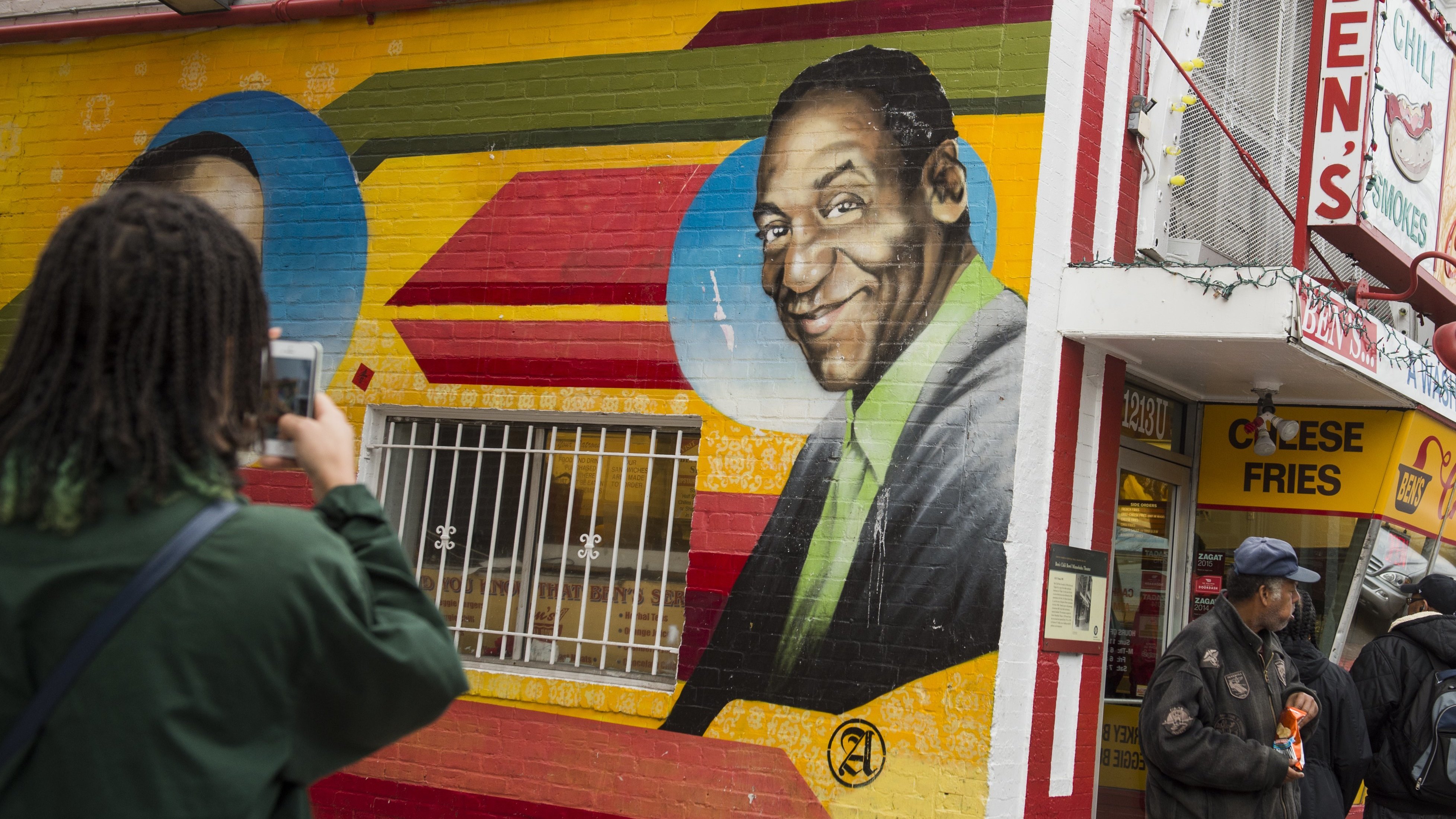 People walk past a mural of comedian Bill Cosby on the side of Ben