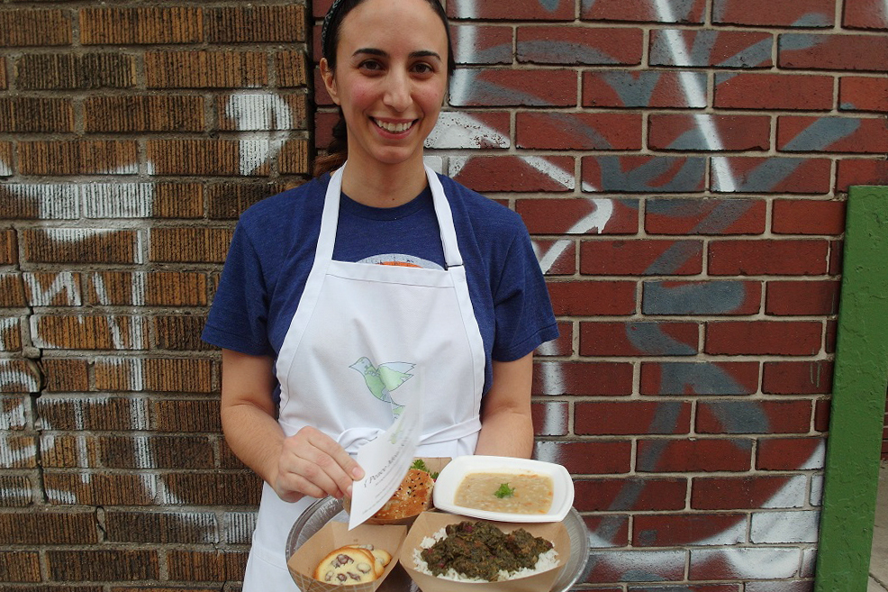 Mana Heshmati, founder of the Detroit-based Peace Meal Kitchen, stands outside of the Detroit City Distillery in Eastern Market during a fundraising event for the ACLU of Michigan. Within two hours, she sold out of her a la carte menu, which included <em>ghormeh sabzi, </em>a Persian beef stew, a vegetarian cream of barley soup, and <em>shirini keshmeshi</em>, delicate rosewater raisin cookies. (Serena Maria Daniels for NPR)