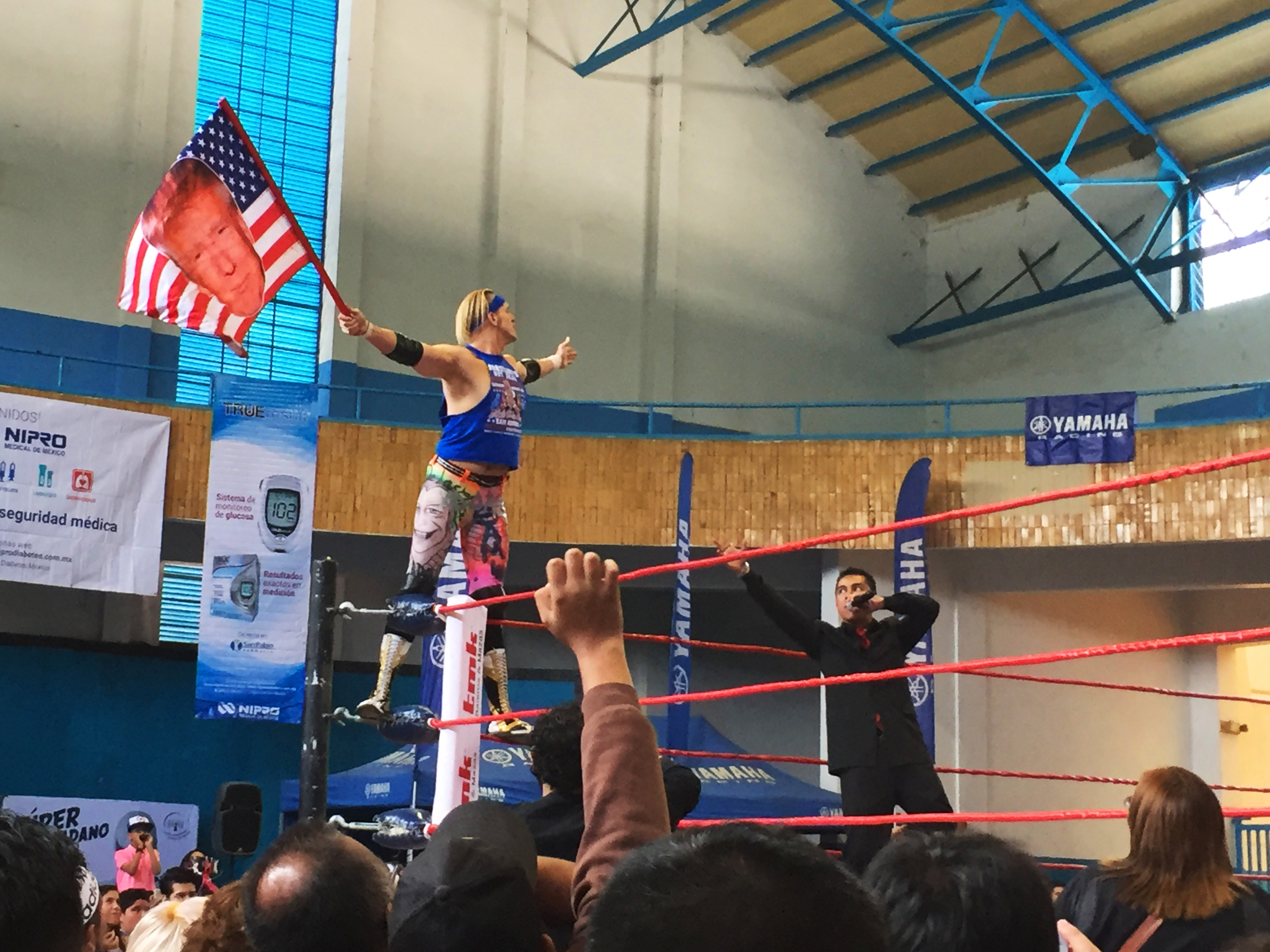 Sam Polinsky, known by his <em>lucha libre</em> wrestling moniker Sam Adonis, enters the ring waving his Trump American flag and riling up the audience in Mexico City. (James Fredrick for NPR)