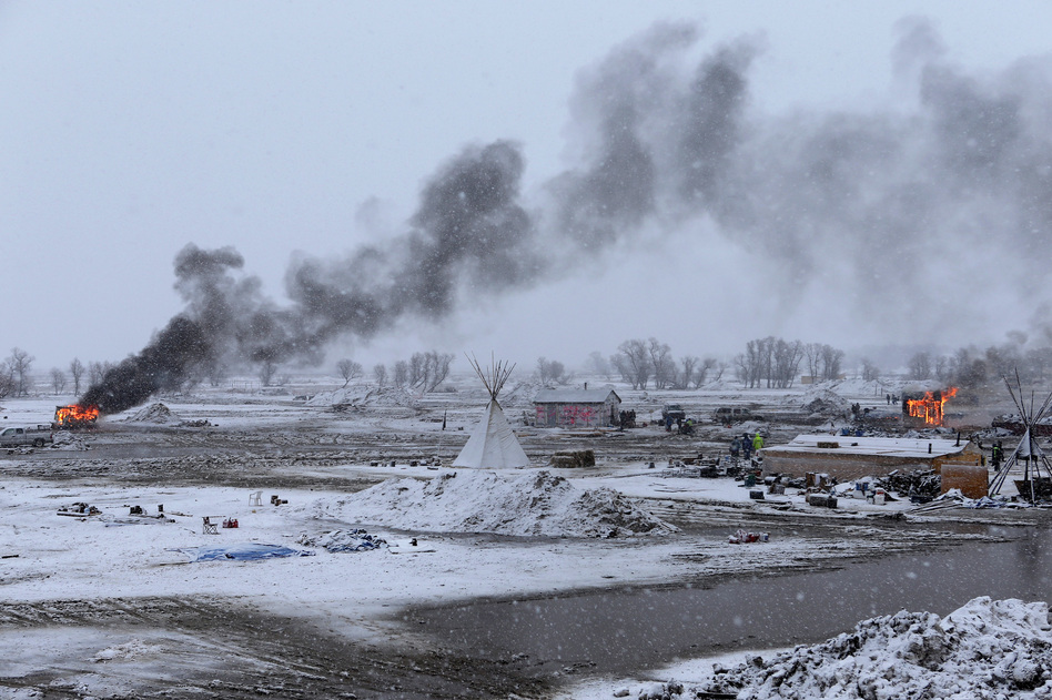 Snow falls on the Oceti Sakowin camp on Wednesday as structures smolder. (Angus Mordant for NPR)