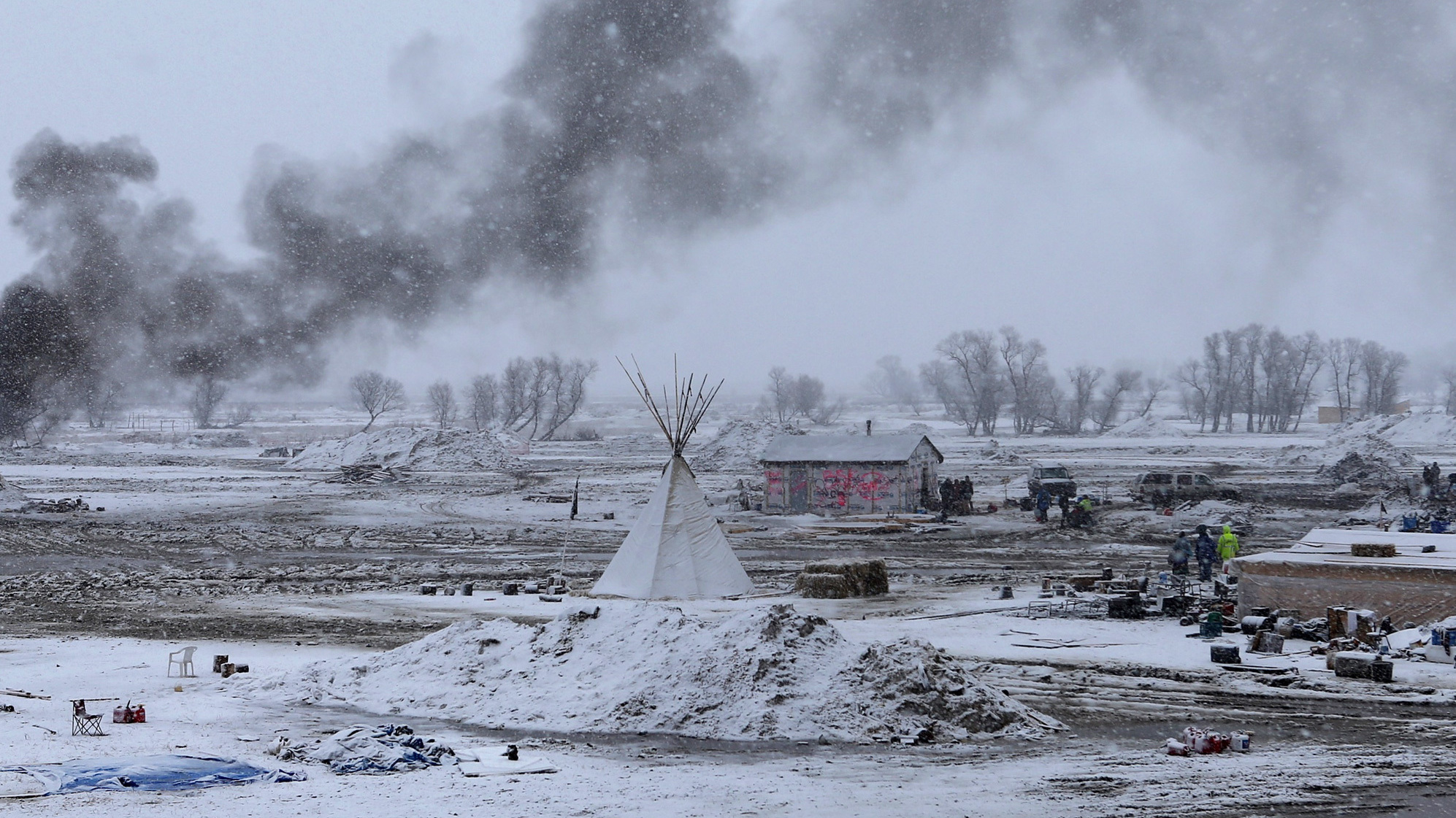 Snow falls on the Oceti Sakowin camp on Wednesday as structures smolder.