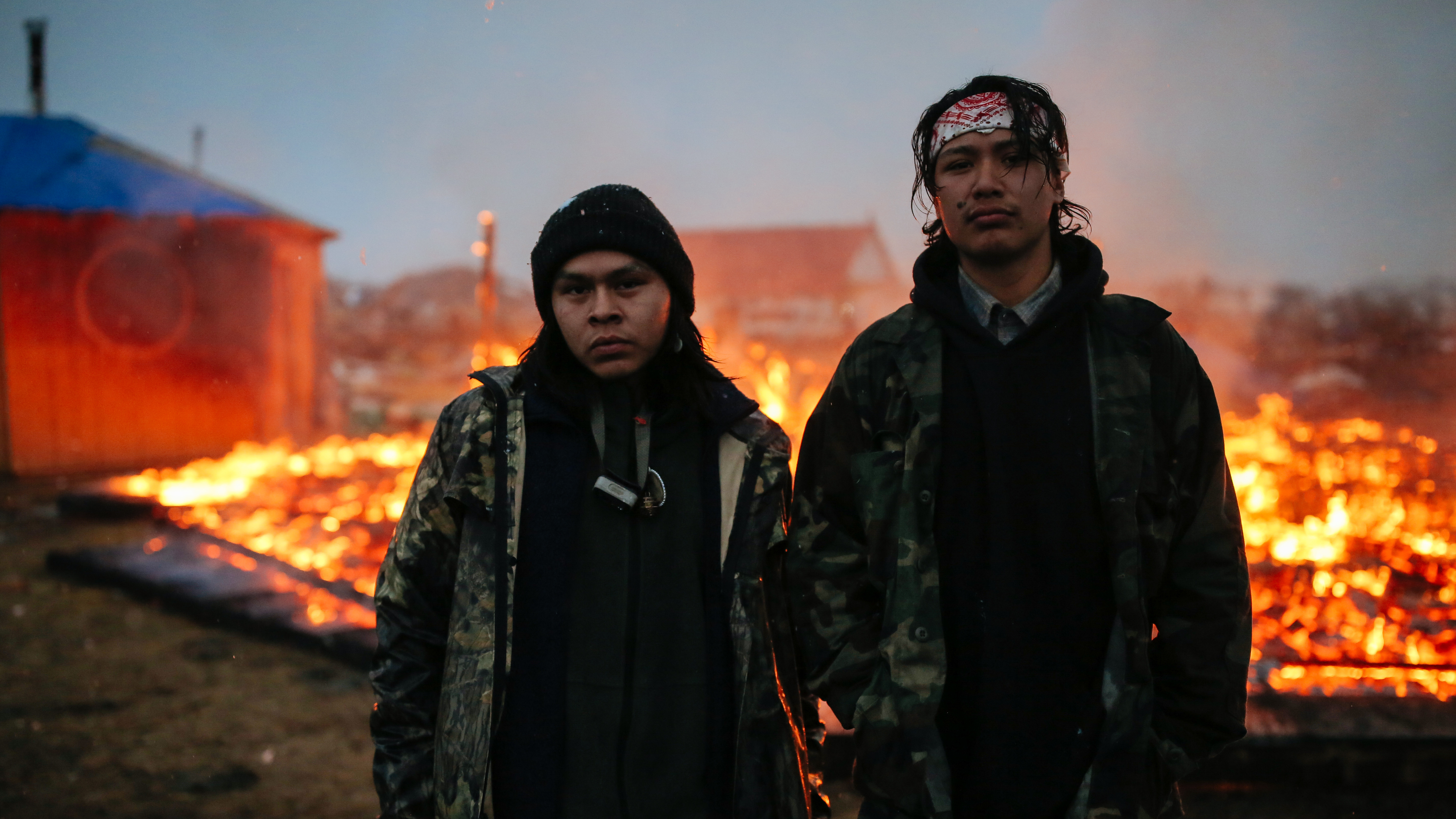 Chanse Zavalla, 22, left, and O'Shea Spencer, 20, right, stand in front of the remains of a hogan structure, set on fire ahead of the Army Corp's deadline to leave the Oceti Sakowin protest camp on February 22, 2017 in Cannon Ball, North Dakota.