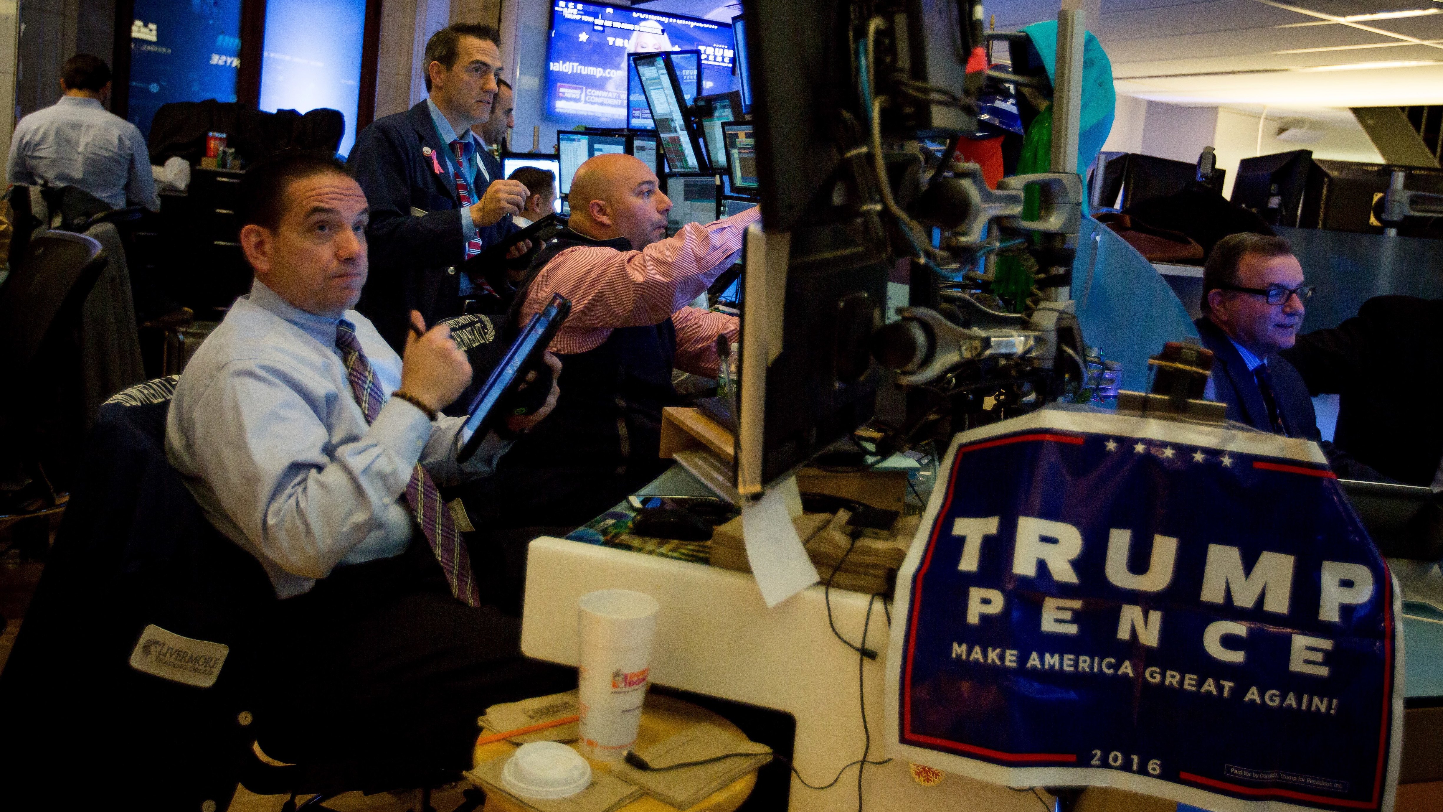 A campaign sign for President Trump and Vice President Pence hangs on a desk while traders work before the opening bell of the New York Stock Exchange the day after the 2016 election. (Bloomberg via Getty Images)
