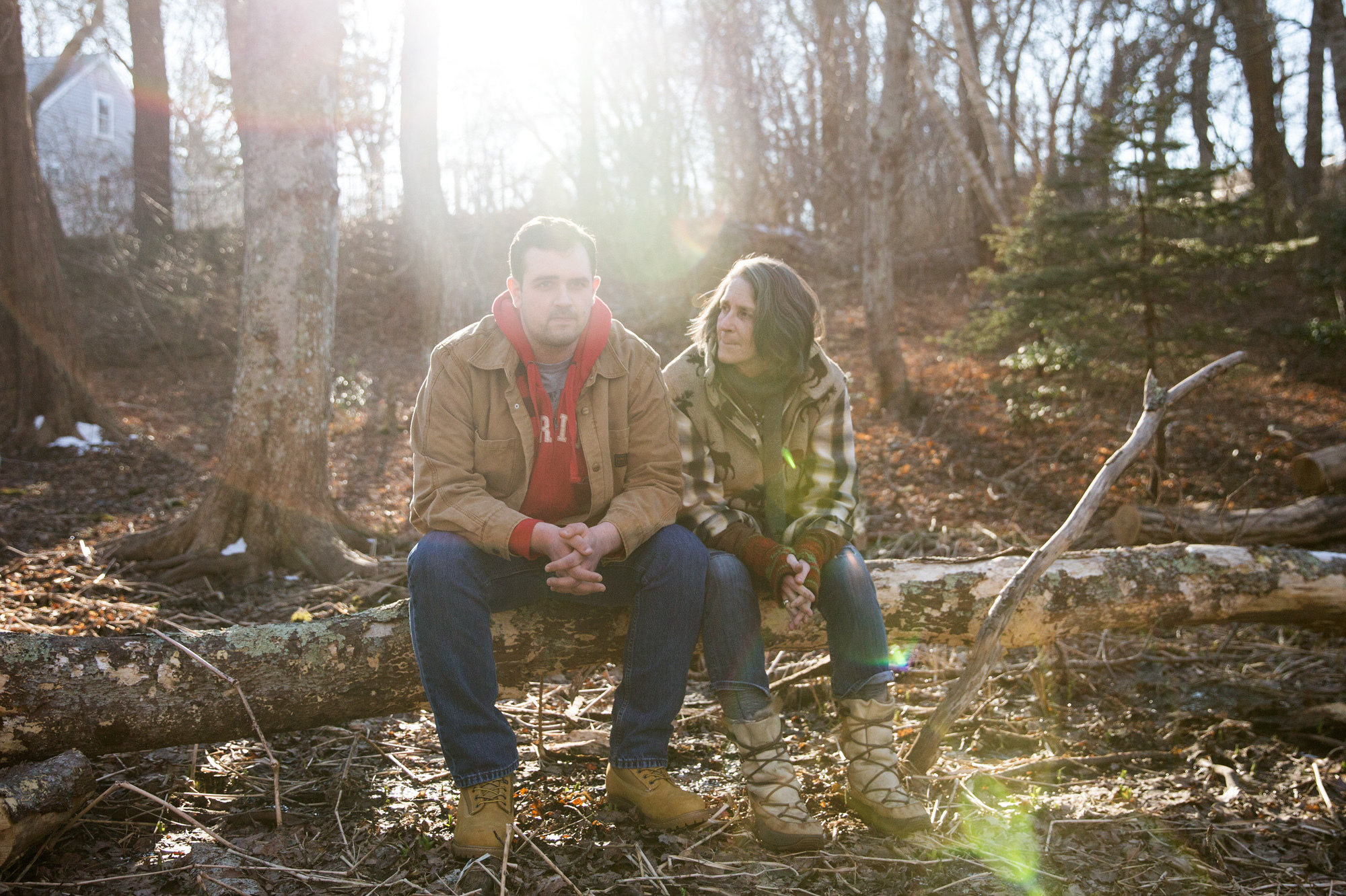 Tucker Lane and his mother, Lynn Cash, sit in the wooded backyard of his home in West Barnstable, Mass. (Kayana Szymczak for NPR)