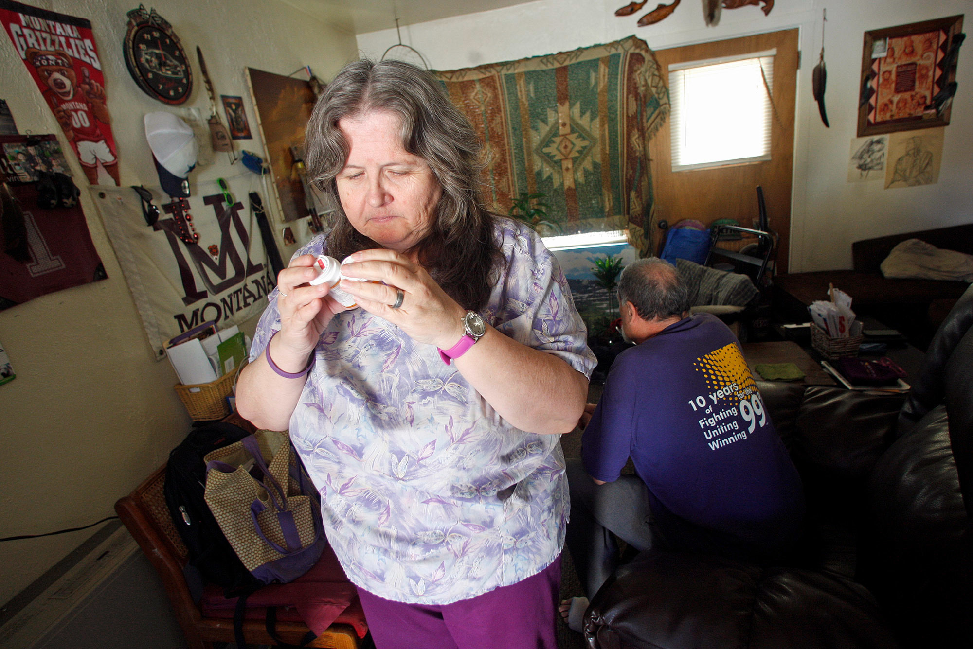 Celeste Thompson, 57, a home care worker in Missoula, Mont., examines a pill bottle in her home. Thompson cares for her husband, and worries that if she loses her Medicaid coverage she won't be able to afford to see a doctor. (Mike Albans for Kaiser Health News)