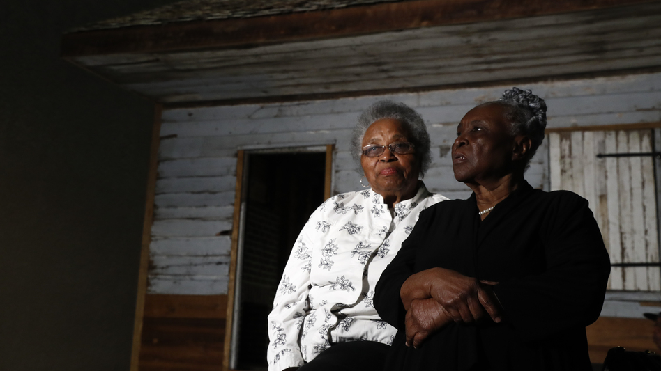 Emily Meggett (left) and Isabell Meggett Lucas sit together at the National Museum of African American History and Culture in front of a slave cabin on display that they grew up in. (Carolyn Kaster/AP)