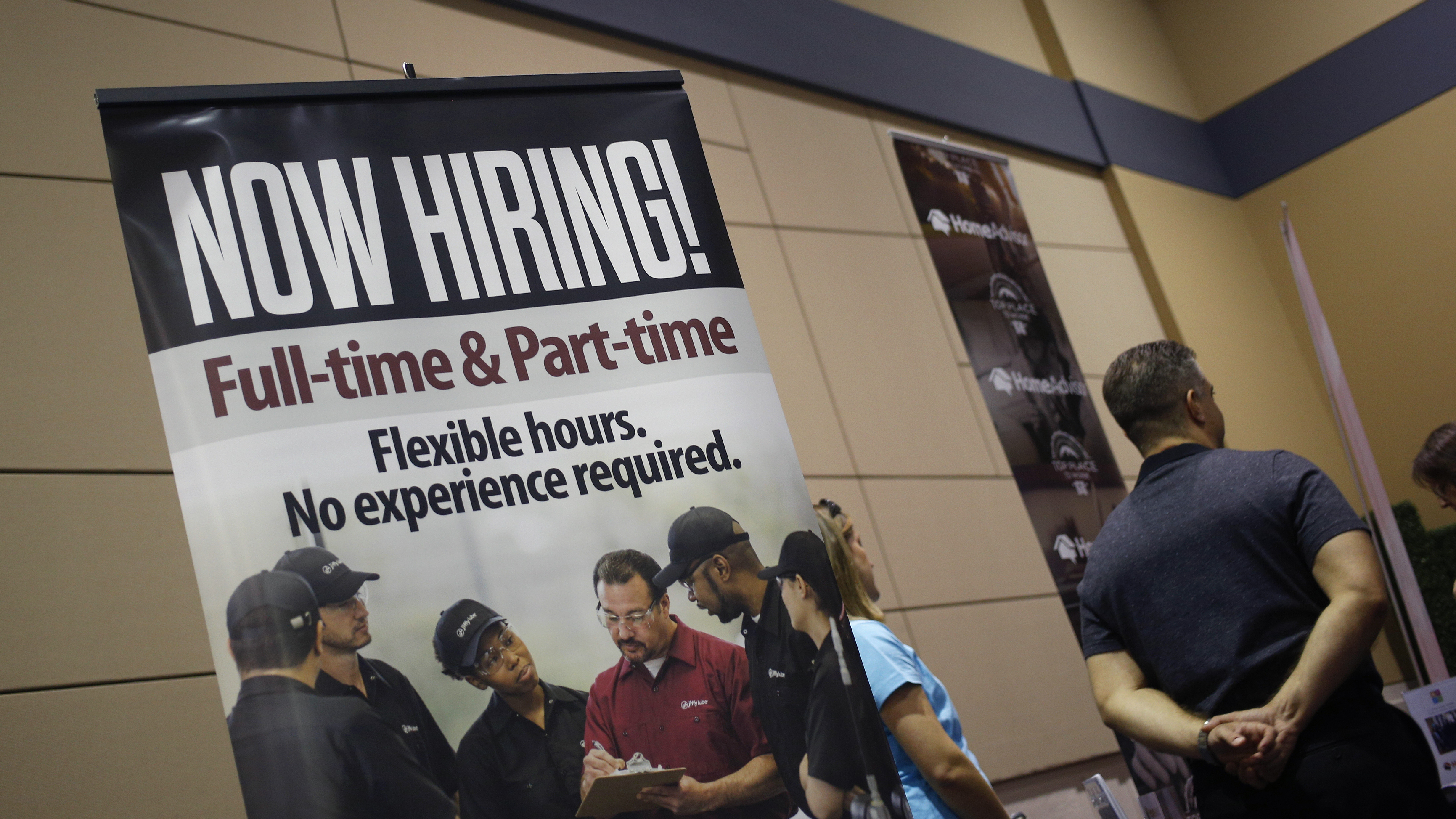 A &quot;Now Hiring!&quot; sign is displayed next to the Jiffy Lube International booth at a jobs fair in Overland Park, Kan., in March. (Bloomberg via Getty Images)