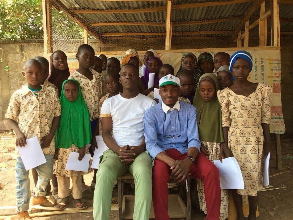Aweofeso Adebola (in white shirt) and Ifeoluwa Ayomide (in cap) pose with some of their students. Zachariah Ibrahim, who dreams of being a pilot, stands behind the girl in the green hijab. Fatima Alidarunge, who wants to be a soldier to fight Boko Haram, is in the blue headgear. (Linus Unah for NPR)