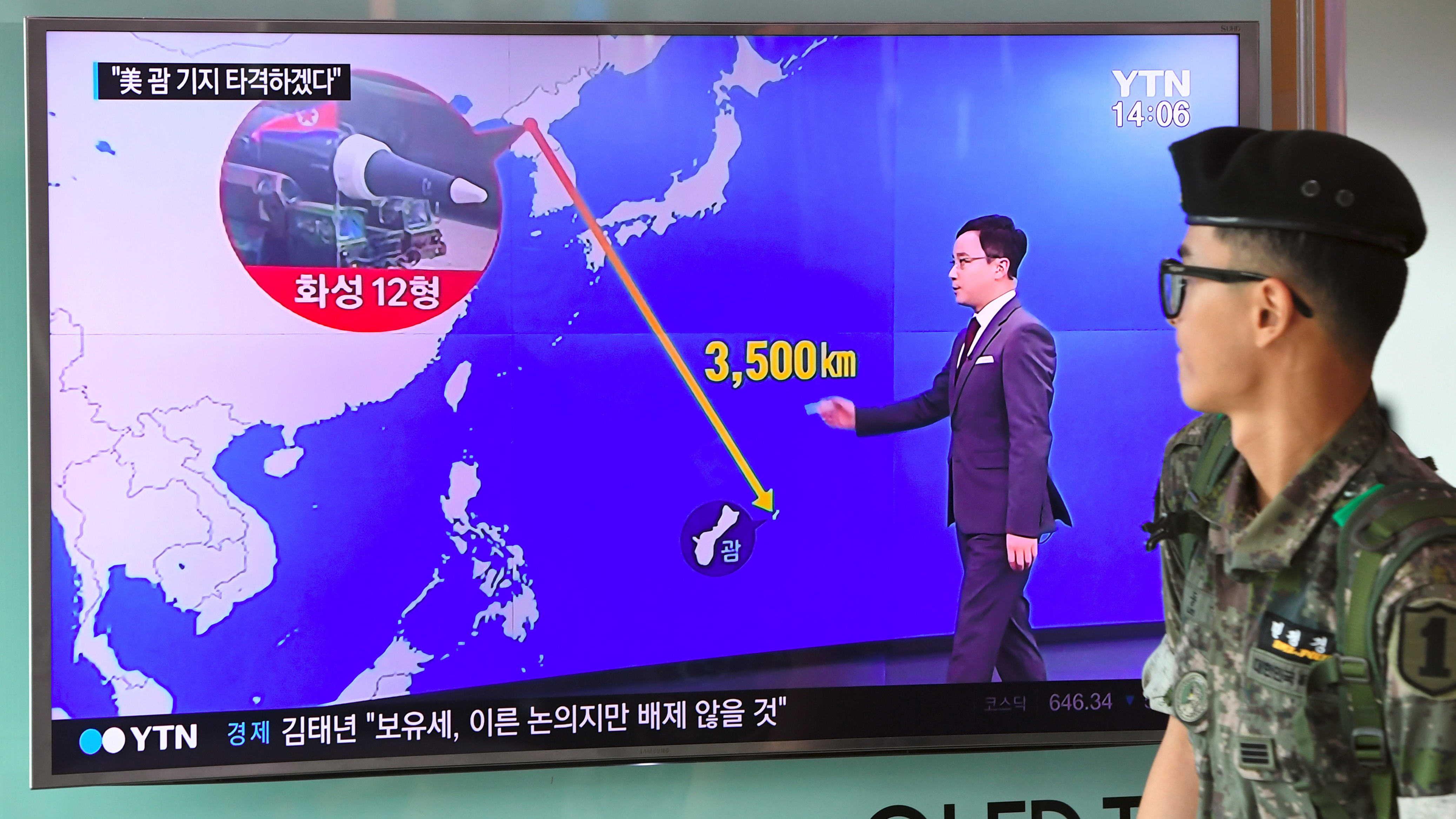 At railway station in Seoul on Wednesday, a South Korean soldier walks past a television screen showing a graphic of the distance between North Korea and the U.S. territory of Guam. (AFP/Getty Images)