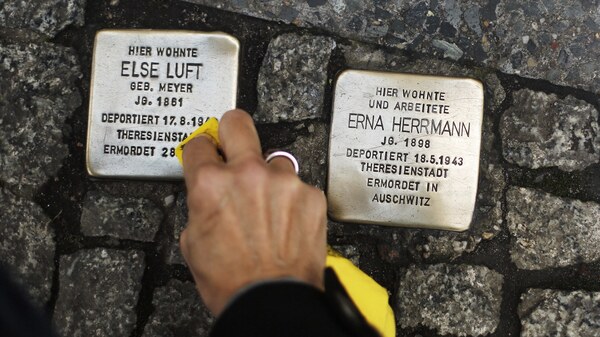 A woman cleans a Stolperstein, or "stumbling stone," placed in the sidewalk in front of houses where victims of the Holocaust lived before they were deported and killed by the Nazis.