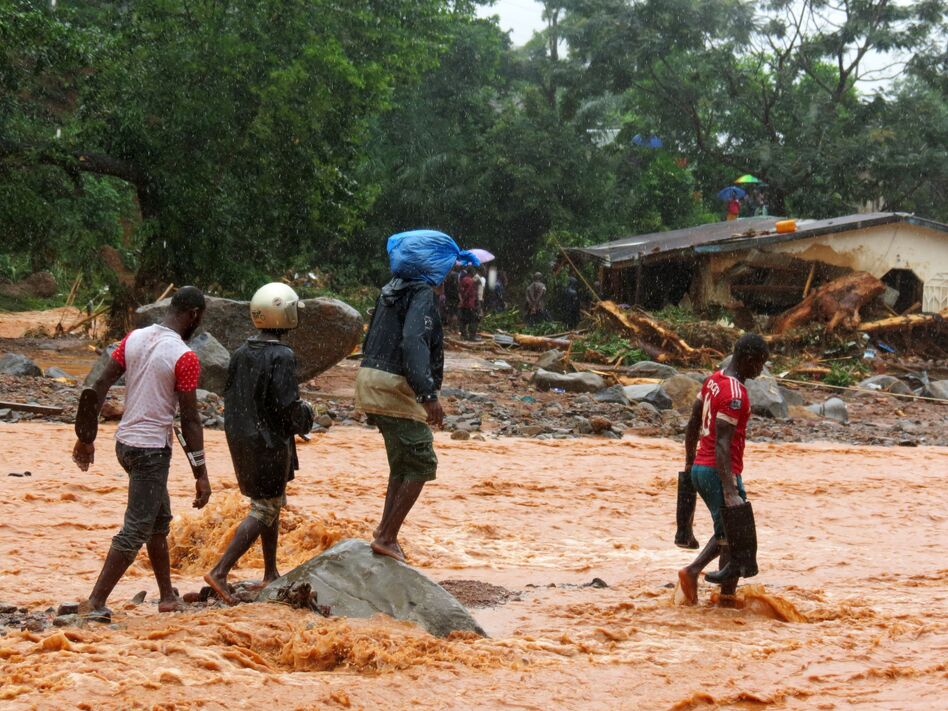 Residents pass a damaged building as they walk through floodwaters on the outskirts of Sierra Leone's capital, Freetown, on Monday. (Saidu Bah /AFP/Getty Images)