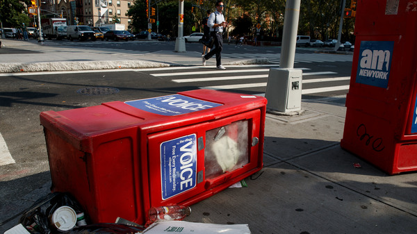 A Village Voice newspaper stand lays on the ground next to garbage in New York City