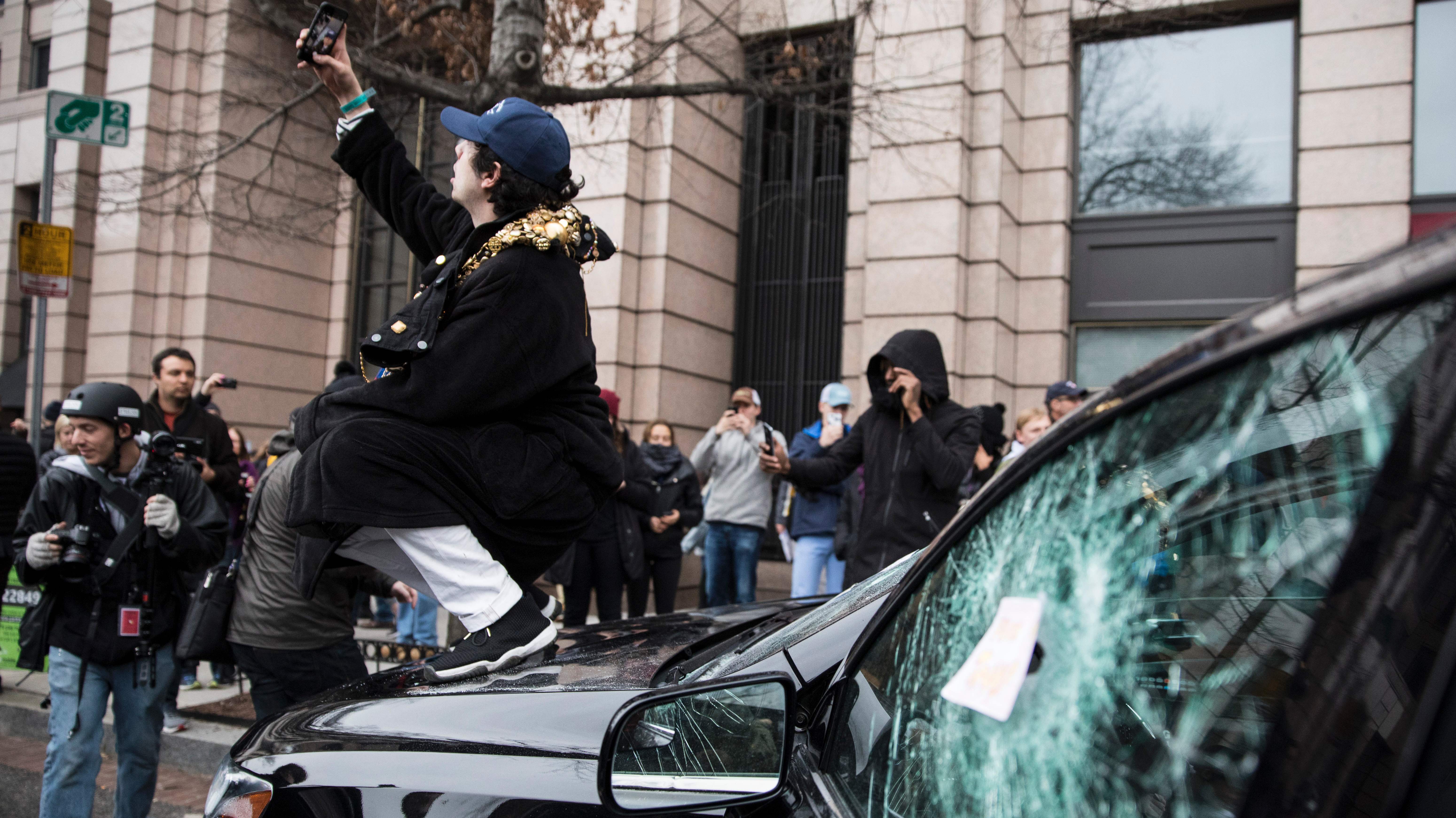 A man takes a selfie on the hood of a destroyed limousine during an Inauguration Day protest against President Trump on Jan. 20 in Washington, D.C. The Department of Justice has been cleared to search through website records related to organizing protests that day. (AFP/Getty Images)