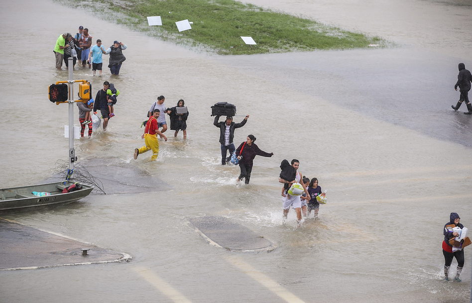 People walk down a flooded street as they evacuate their homes in Houston on Monday. (Joe Raedle/Getty Images)