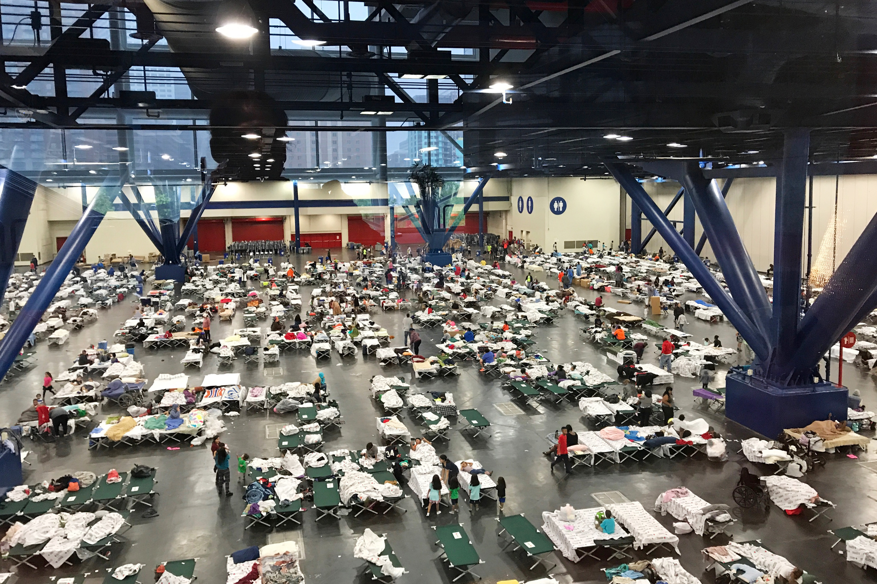 People gather around cots inside the George R. Brown Convention Center in Houston as they take shelter from the flooding on Monday. (NPR)