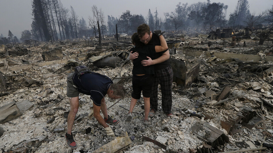 Michael Pond, left, looks through ashes as his wife Kristine, center, gets a hug from Zack Thurston, their daughter's boyfriend, while they search the remains of their home destroyed by fires in Santa Rosa, California. (Jeff Chiu/AP)