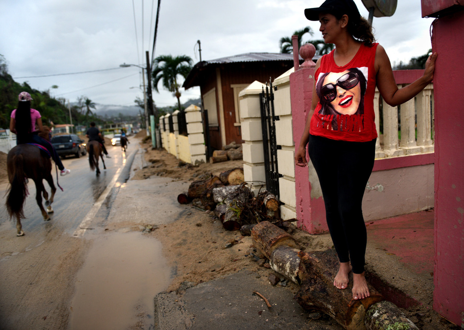 Residents handle aftermath of hurricane with resilience, humor and spirit. Jaylyn Rosario stands on makeshift barrier to prevent flooding of her home on Avenida Esteves, piled high with sand and debris washed in from a creek. (Carol Guzy for NPR)