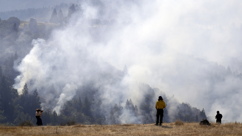 A firefighter (center) and two onlookers watch a smoldering wildfire from a hilltop in Oakville, Calif., on Sunday. (Marcio Jose Sanchez/AP)