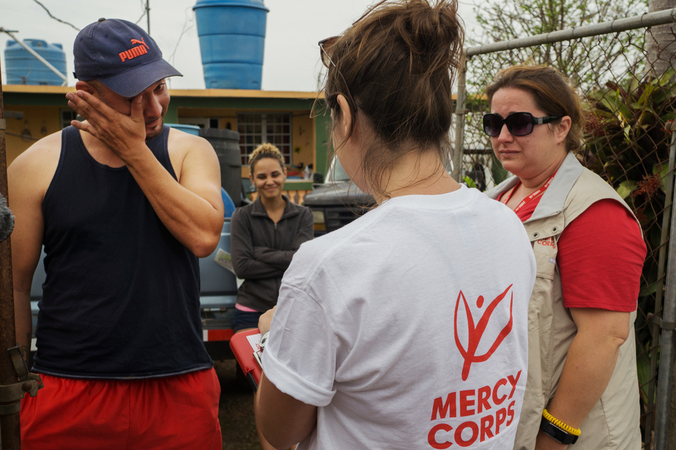 Argenis Ramos, 34, wipes a tear while answering questions for a field research survey by Mercy Corps staffers Alexa Swift (center) and Jill Morehead. Ramos' wife, Karian Batista, looks on. (Angel Valentin for NPR)