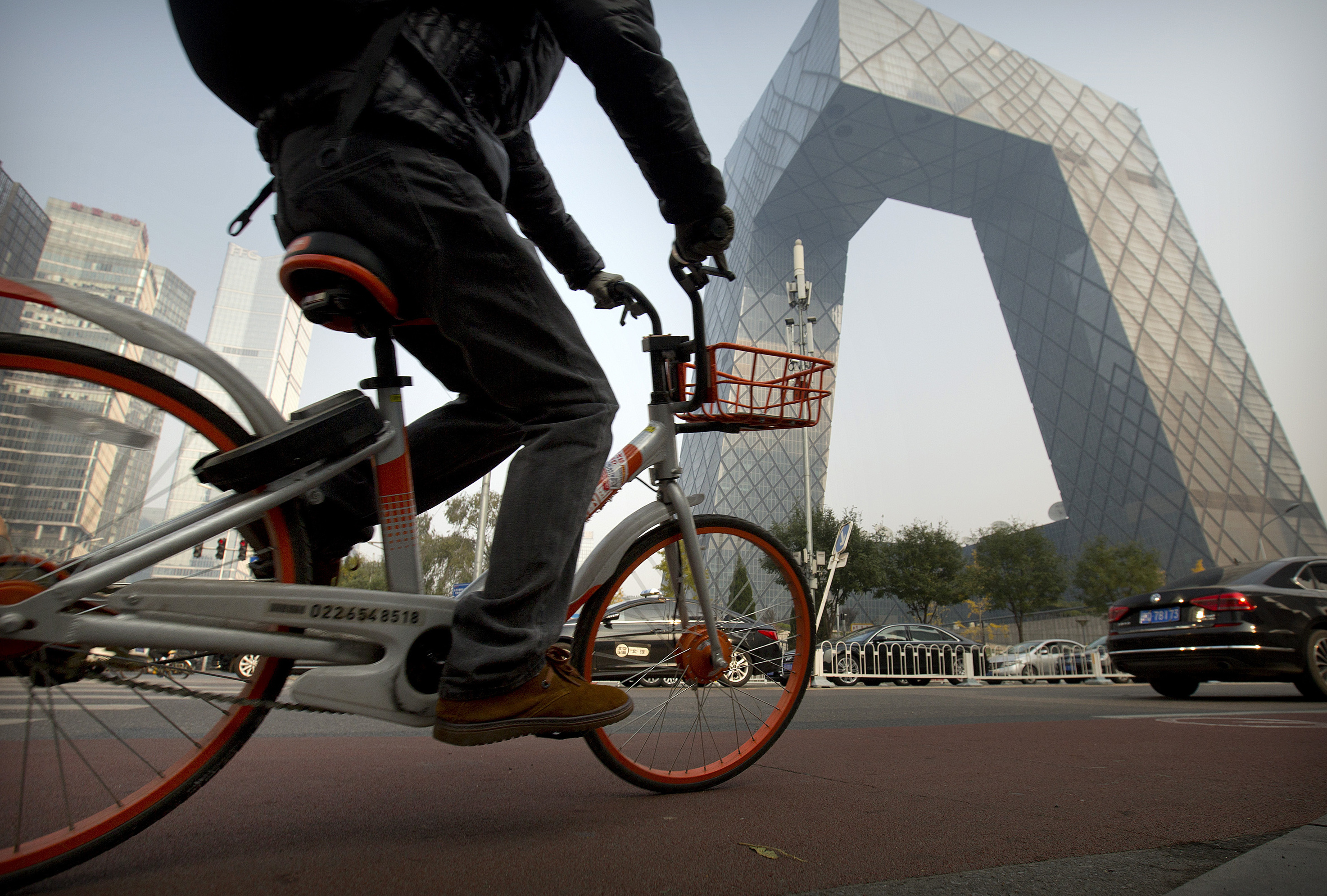 A man rides a Mobike bicycle past the CCTV Headquarters building in Beijing. (AP for NPR)