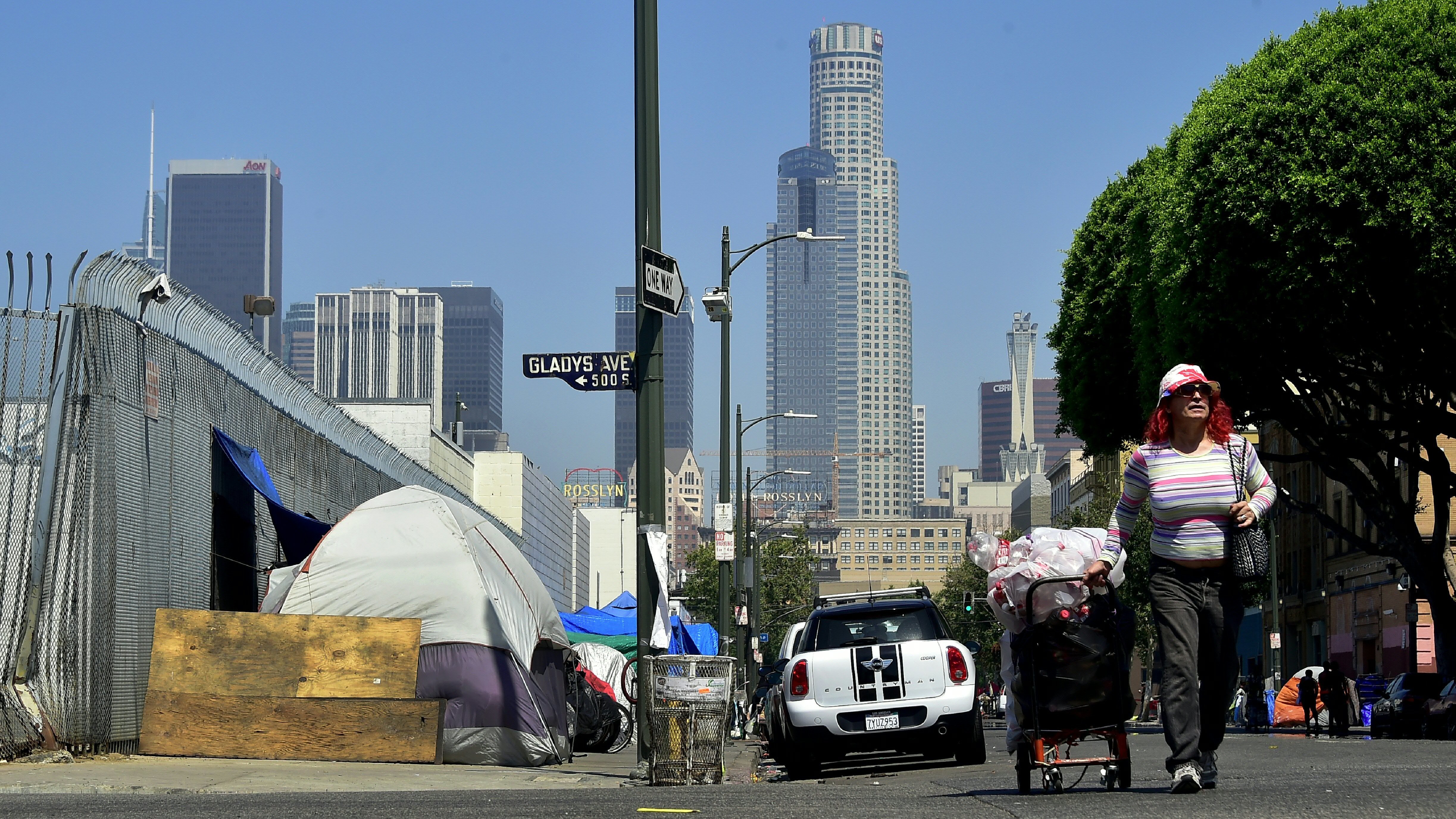 A woman pushes her cart full of belongings along the street past tents on the sidewalk near skid row in downtown Los Angeles in June. (AFP/Getty Images)