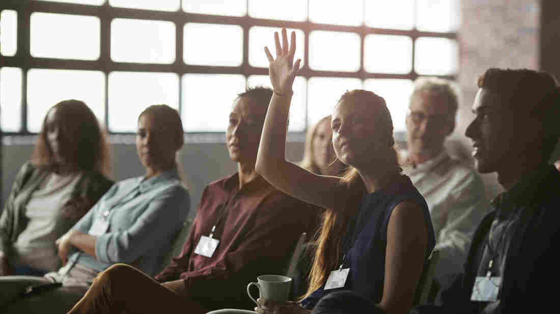 Businesswoman with raised hand at convention in New York style auditorium