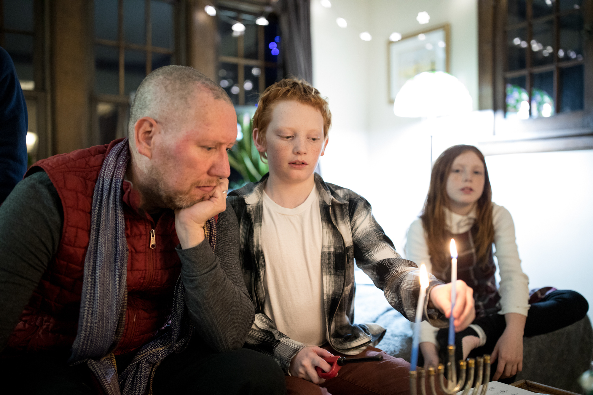 Carl Luepker, his son Liam, 12, and daughter Lucia, 11, light the menorah during Hanukkah in their home in Minneapolis, Minn. Carl and Liam both have a degenerative nerve disorder called dystonia. (Jenn Ackerman for NPR)