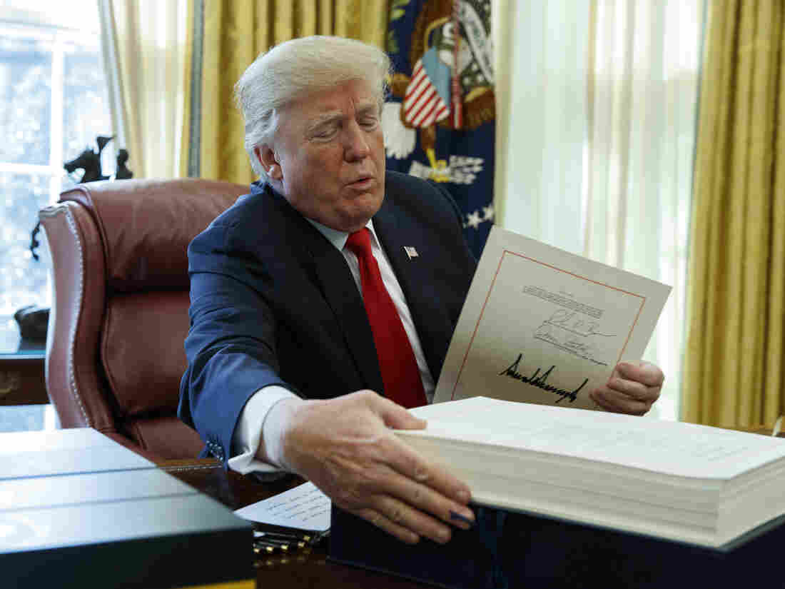 President Donald Trump grabs a box containing the tax bill after signing it in the Oval Office of the White House, Friday, Dec. 22, 2017, in Washington. (AP Photo/Evan Vucci)