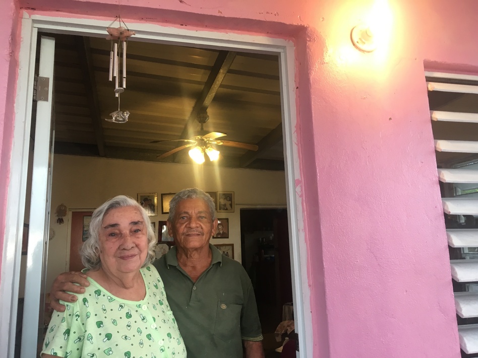 Rosa Cruz and Luis Felipe Colón standing beneath the newly illuminated light on their front porch. The couple had been without electricity for four months. (Adrian Florido/NPR)