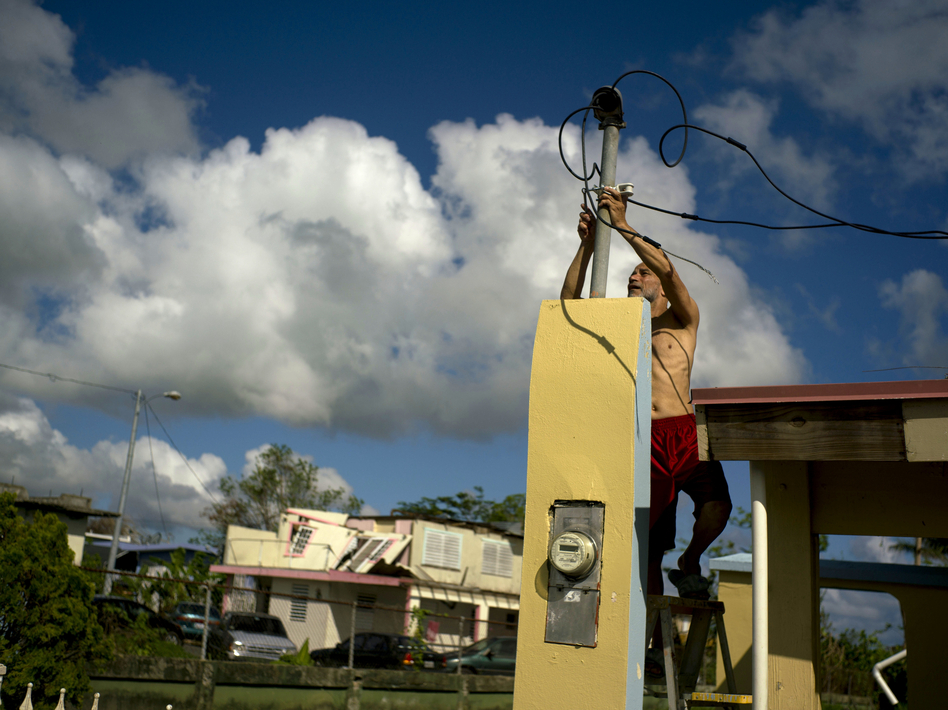 In a photograph taken in October, a resident tries to connect electrical lines downed by Hurricane Maria in preparation for when electricity is restored in Toa Baja, Puerto Rico. (Ramon Espinosa/AP)