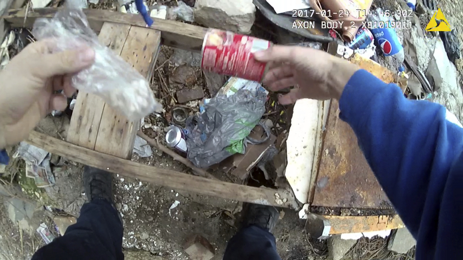 Body camera footage appears to show Officer Richard Pinheiro placing a can with drugs in a trash pile and returning later to seemingly discover it. A grand jury indicted him Tuesday. (Baltimore Police Department via AP)