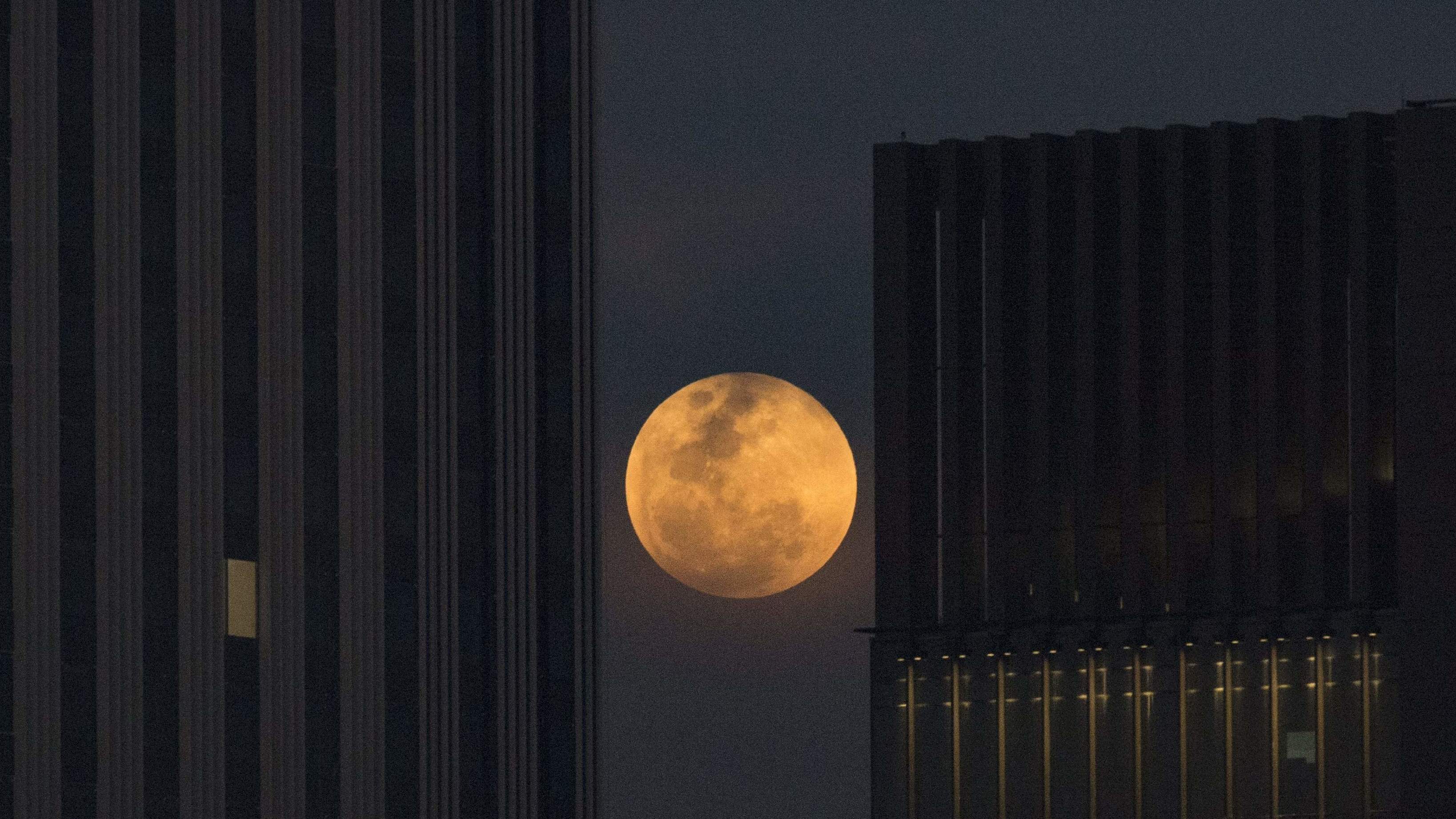 The moon rises between two office buildings in Bangkok, Thailand.