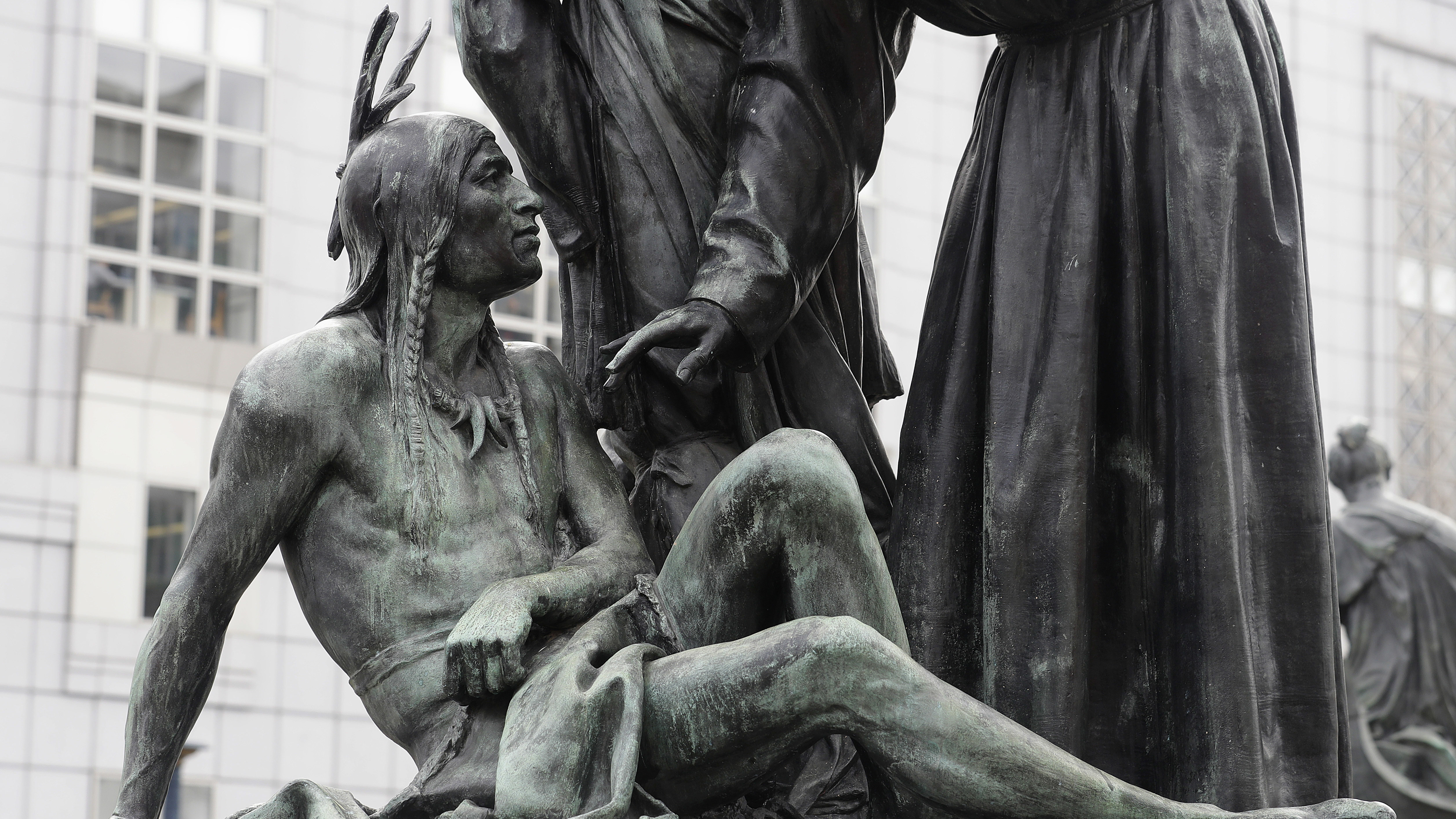A statue of a Native American sitting below a vaquero and a missionary in San Francisco.