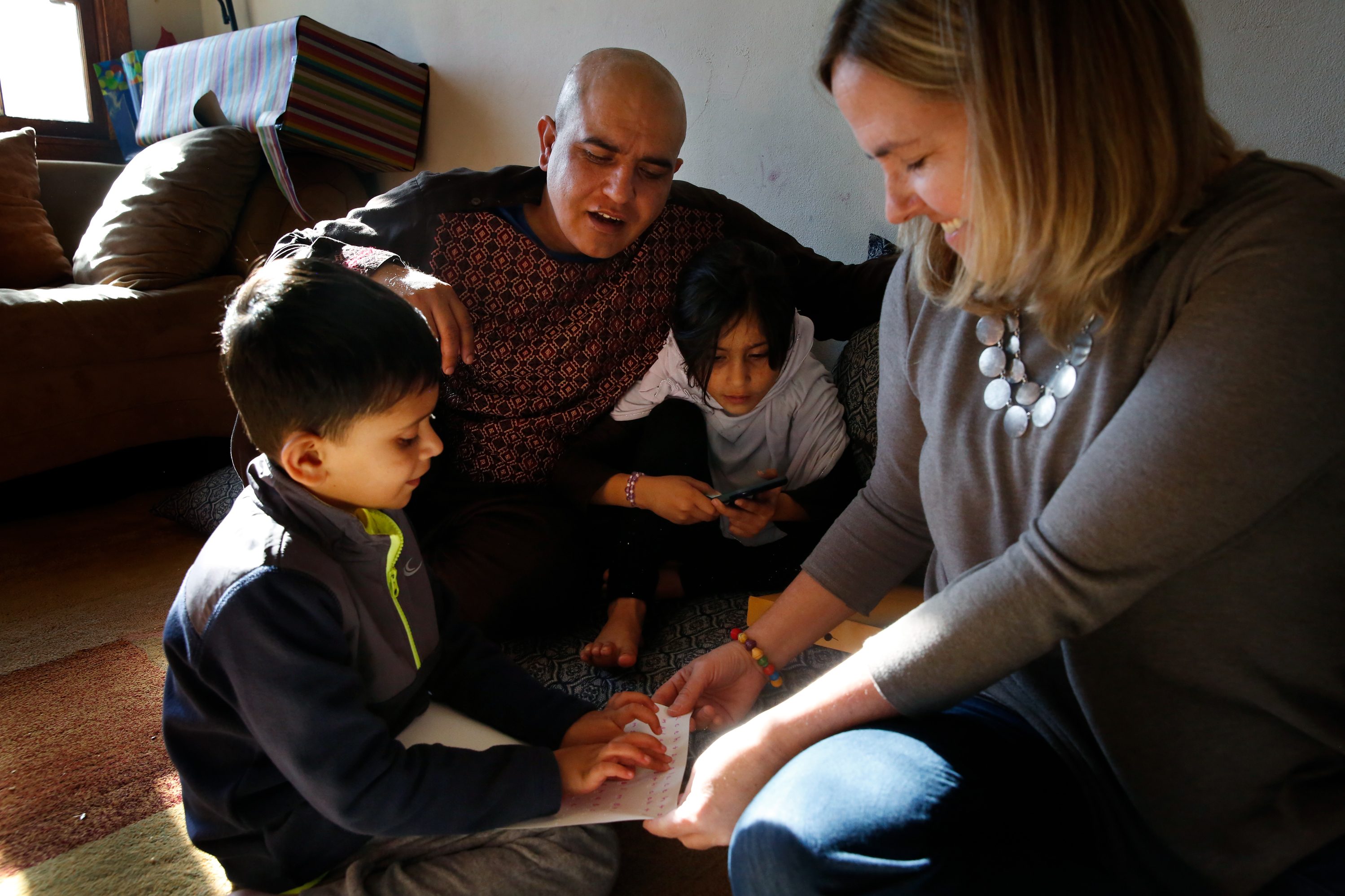 Cathy Meaney (right), a volunteer with International Neighbors, sits with Rahim Nishat and two of his children in the Nishats' apartment in Charlottesville, Va. The Nishat family is from Afghanistan. (NPR)