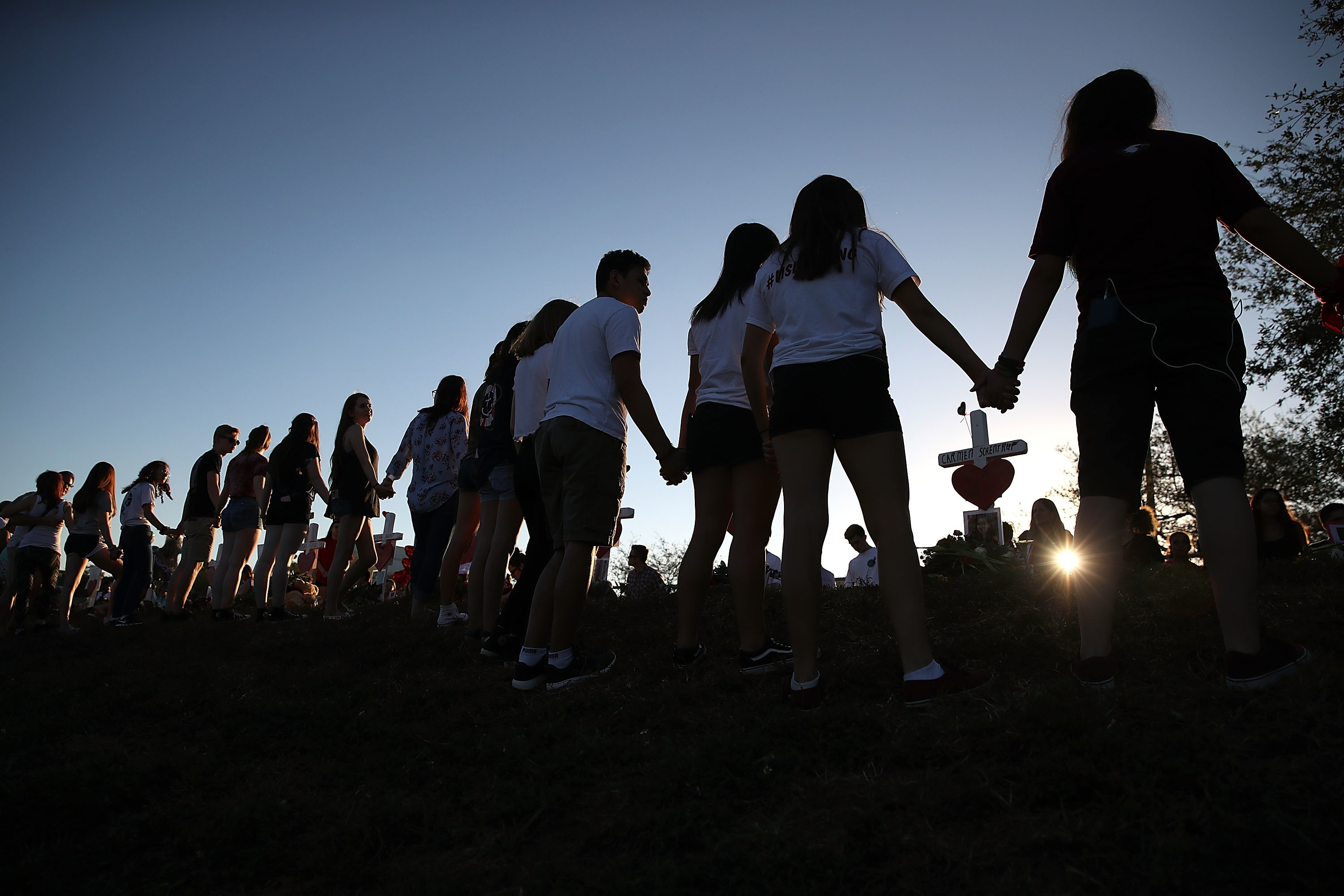 Students and family members hold hands around a makeshift memorial in front of Marjory Stoneman Douglas High School in Parkland, Fla., where 17 people were killed on Feb. 14. (Getty Images)