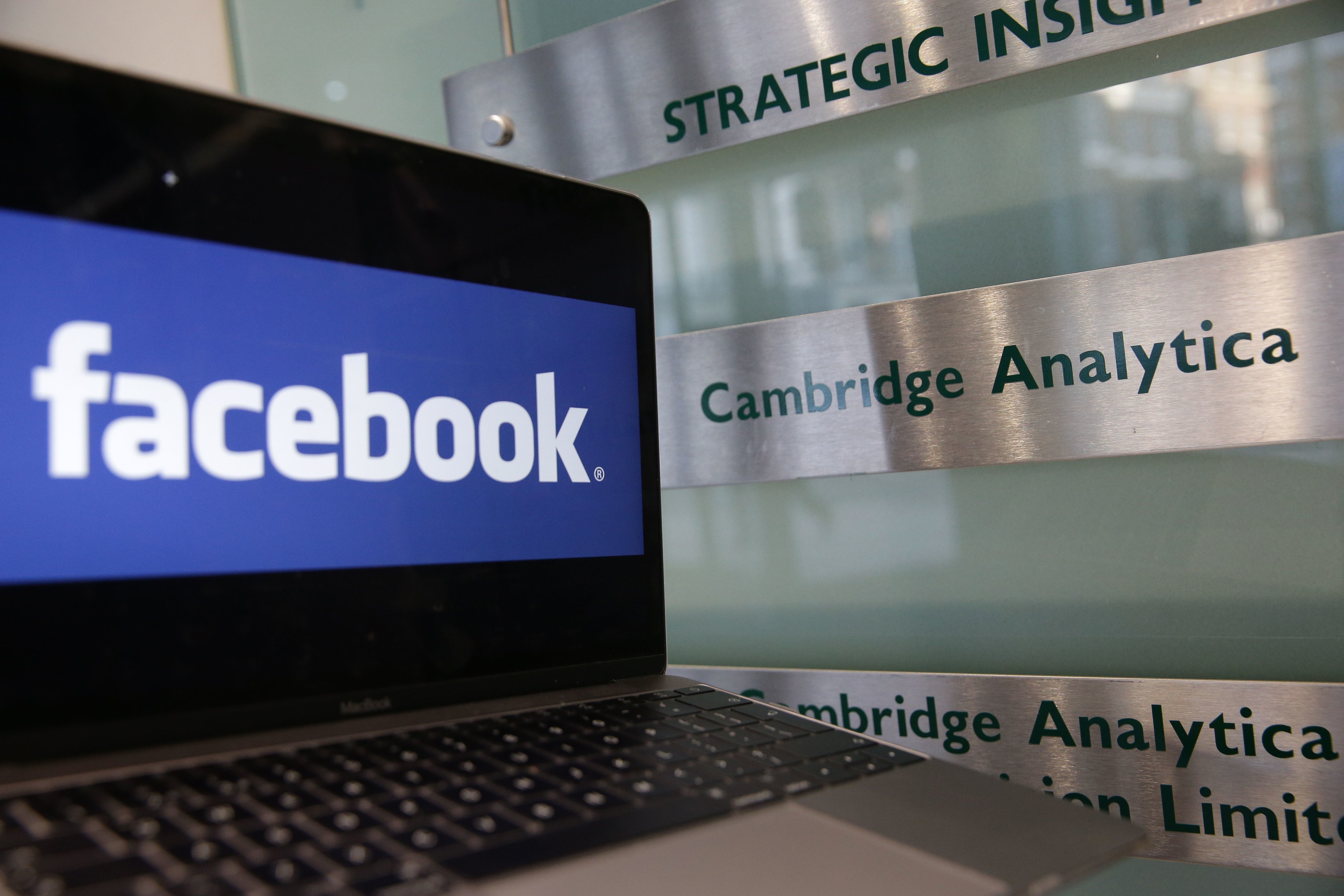 A laptop showing the Facebook logo is held alongside a Cambridge Analytica sign at the entrance to the London offices of Cambridge Analytica. The company's acting CEO, Alexander Tayler, is stepping down, and is the second CEO out since the data sharing scandal broke. (AFP/Getty Images)