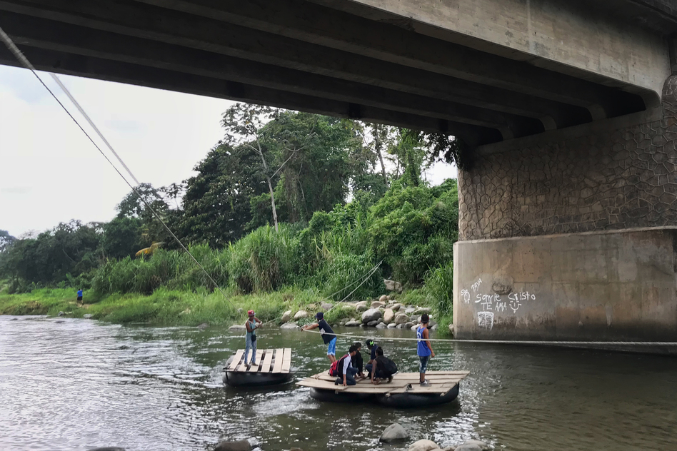 Migrants and day laborers cross the Suchiate River, which divides Mexico and Guatemala. The crossing happens despite immigration officials working on the bridge above. (James Frederick for NPR)