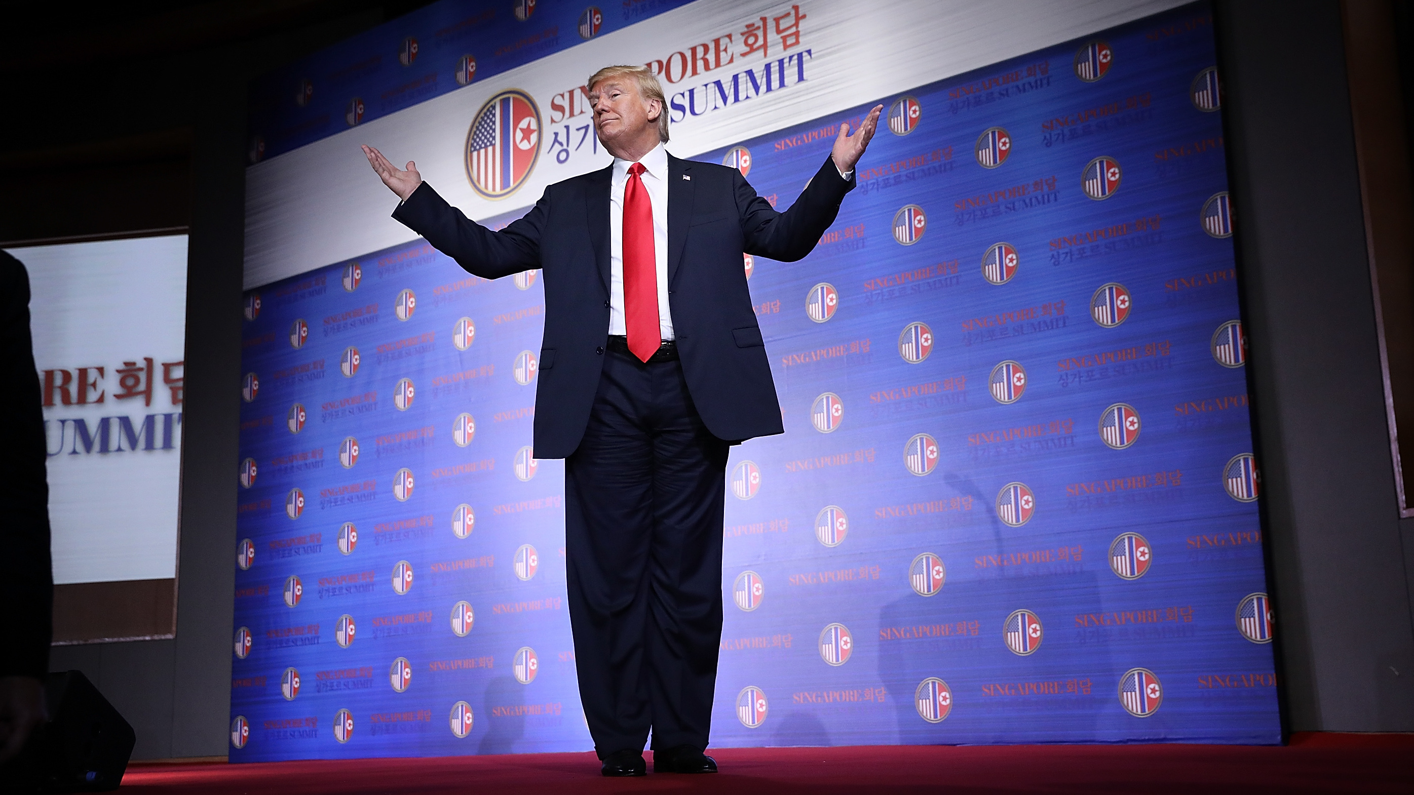 President Trump stands on the podium in Singapore with his arms outstretched and answers a final question from reporters. Back in the U.S., he was flexing his muscles in GOP primaries.