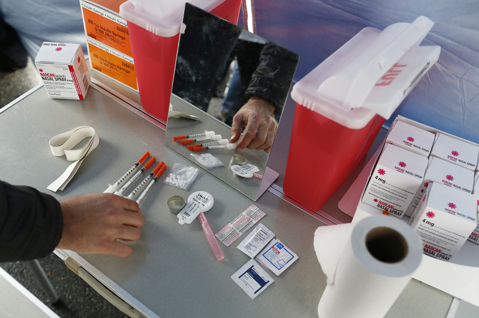 A visitor to the Harvard School of Public Health's mock safe injection setup checks out the items on the demonstration table set up underneath a tent on the quad near the medical school in Boston on April 30, 2018.