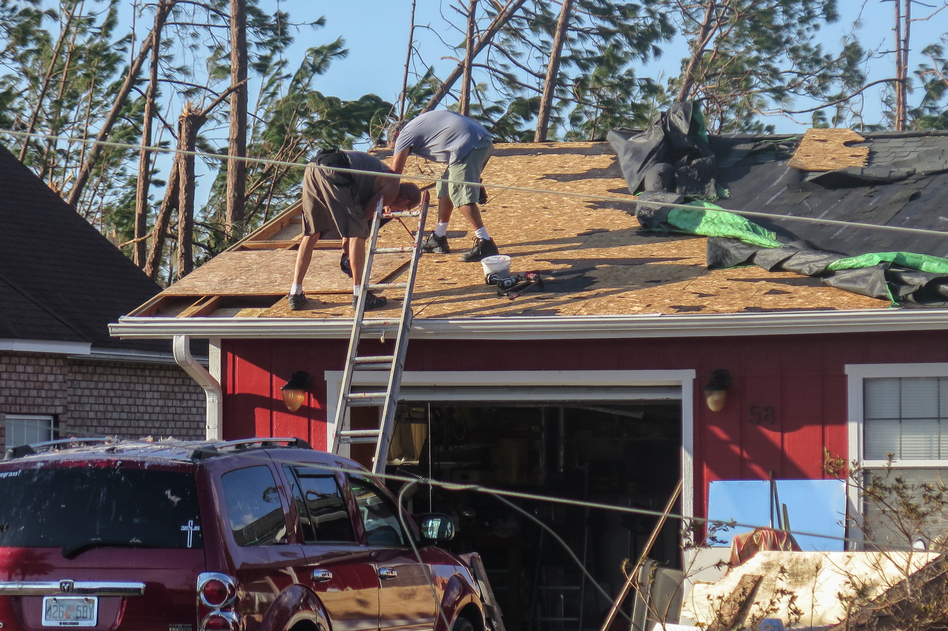 Lance Erwin works with a neighbor in Mexico Beach, Fla., to repair parts of his roof after it was blown off by Hurricane Michael. Rules are looser in the Pandhandle, allowing construction that couldn't stand up to the storm's 155 mph winds. (Greg Allen/NPR)