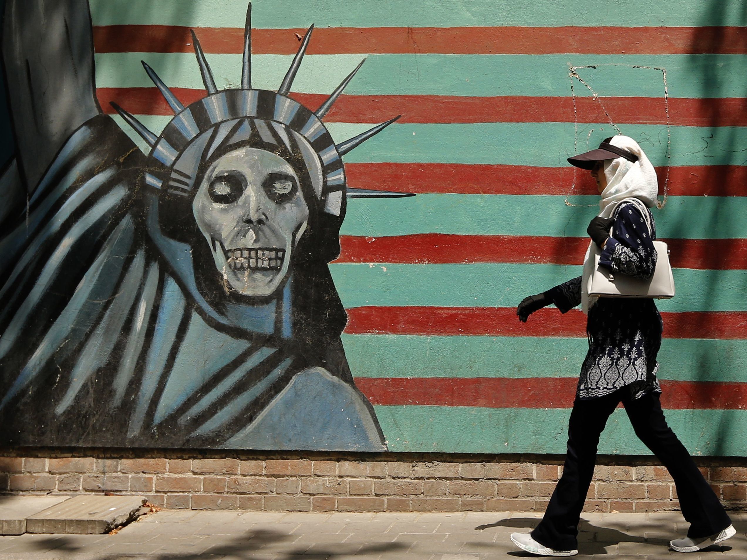 An Iranian woman walks past the former U.S. Embassy in Tehran, which bears a mural depicting the Statue of Liberty with a dead face. With just days to go until the U.S. plans to snap more sanctions back into place, questions linger about what the move spells for the world. (AFP/Getty Images)