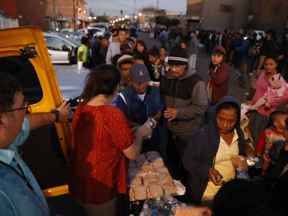 Well-wishers distribute food to migrants outside of a sports complex where more than 5,000 Central Americans are sheltering, in Tijuana, Mexico. President Trump wants the migrants to stay in Mexico while their asylum claims play out in U.S. immigration court. (Rebecca Blackwell/AP)