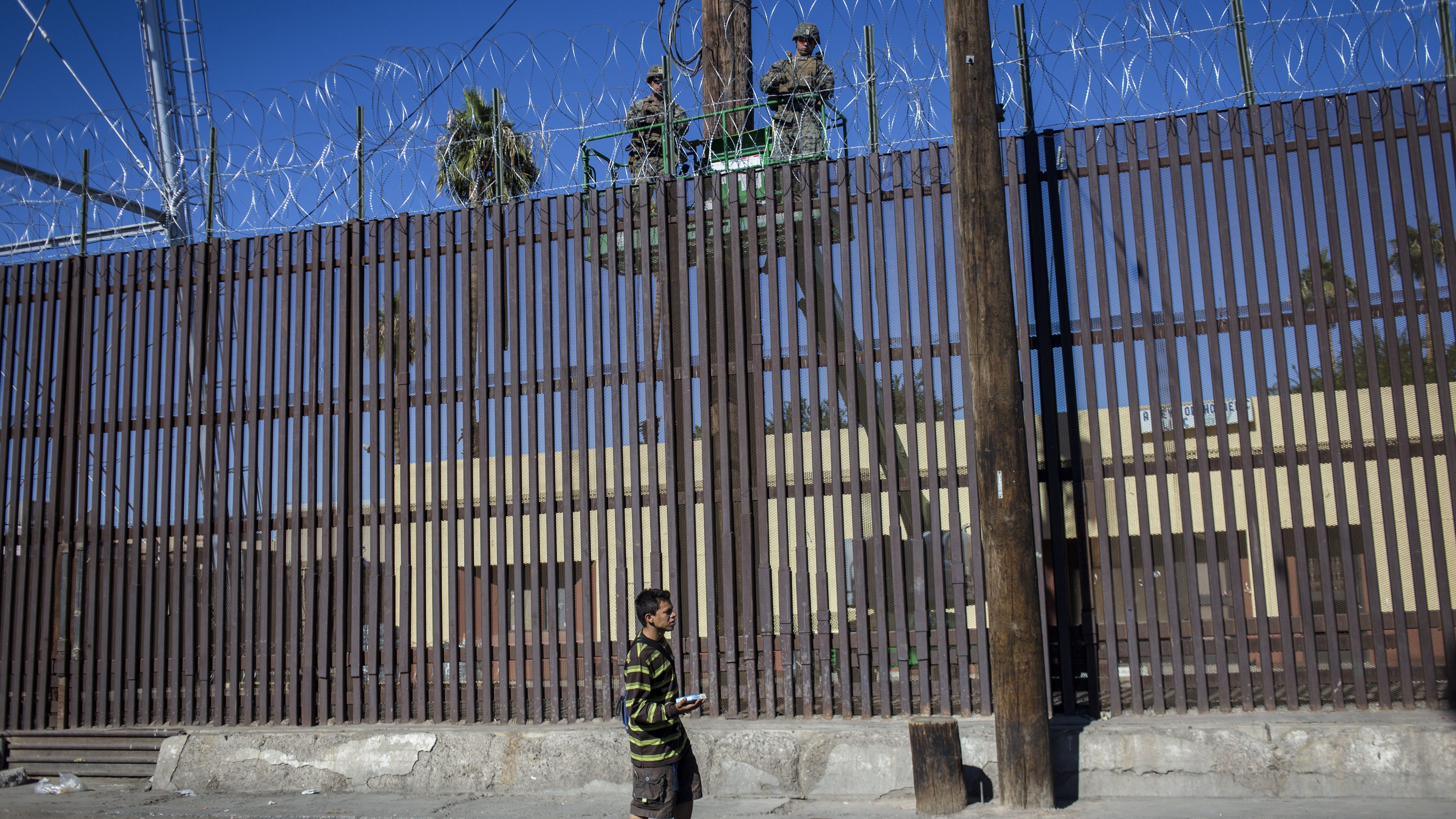 Defense Secretary Jim Mattis will likely reduce the number of active-duty U.S. troops who are currently deployed at the Mexico border, from around 5,900 to around 4,000. Here, a street candy seller walks in Mexicali, Mexico, while U.S. Army soldiers fortify a U.S.-Mexico border fence with barbed wire.