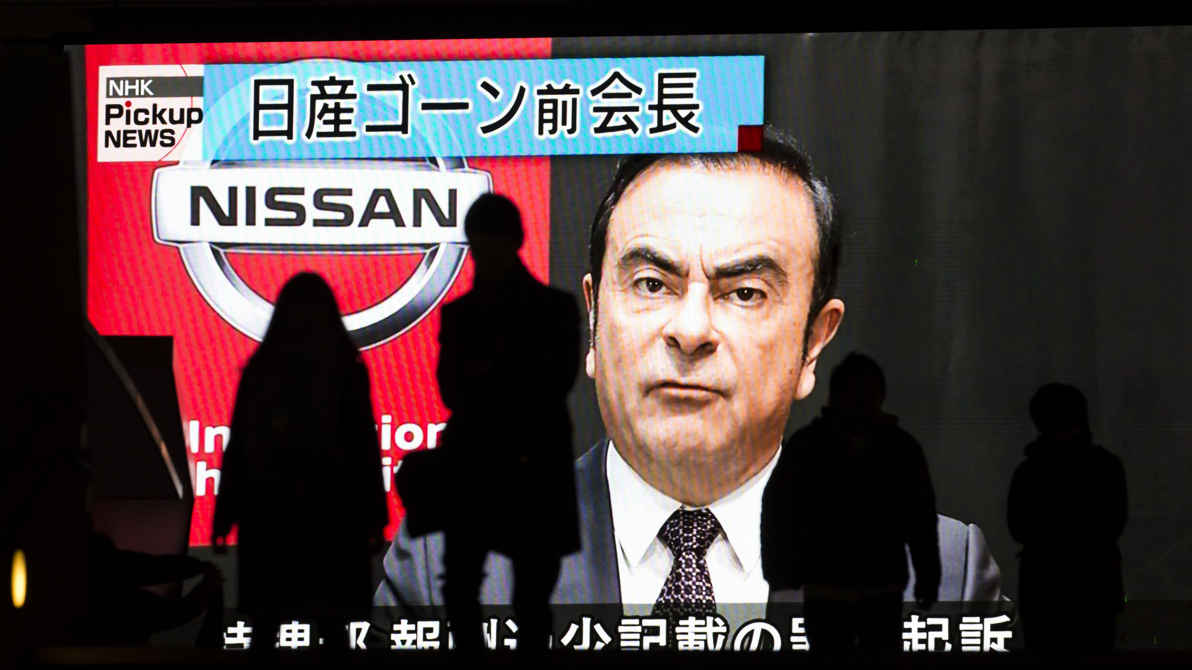 Pedestrians walk in front of a monitor showing an image of former Nissan Motor Co. Chairman Carlos Ghosn on Monday in Tokyo, Japan. Ghosn, a veteran of the auto industry, was charged on Monday for financial misconduct after he was arrested in Tokyo last month on accusations he underreported his compensation to authorities. (Getty Images)