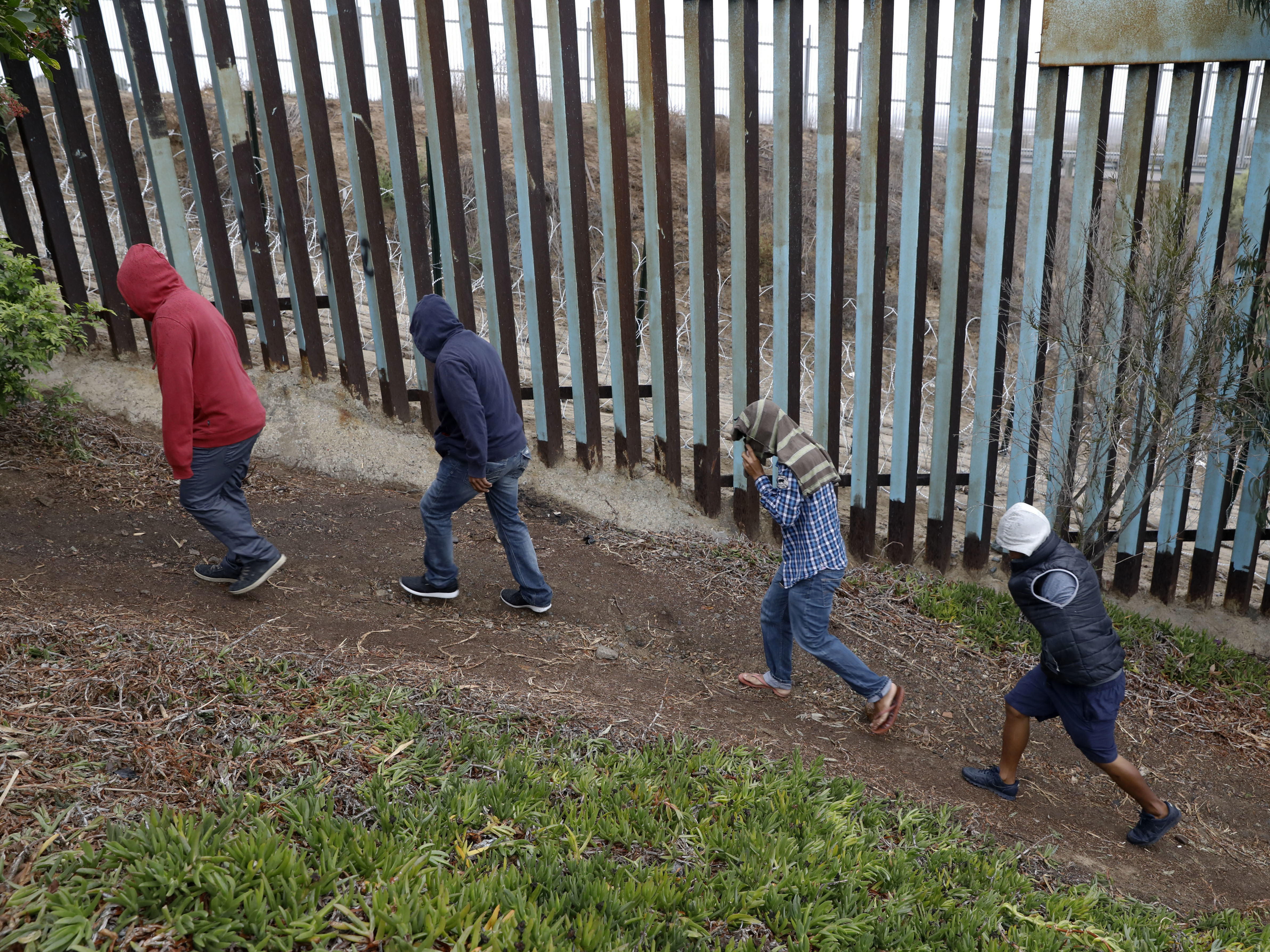 Central American migrants walk along the U.S. border fence looking for places to cross, in Tijuana, Mexico.